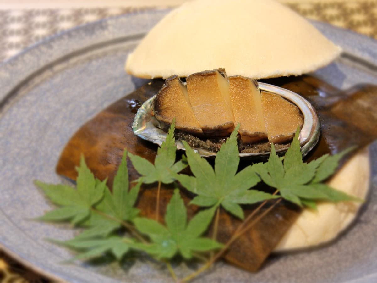 Kaiseki course of simmered Bocchan-jima abalone garnished with fresh maple leaves on a ceramic plate