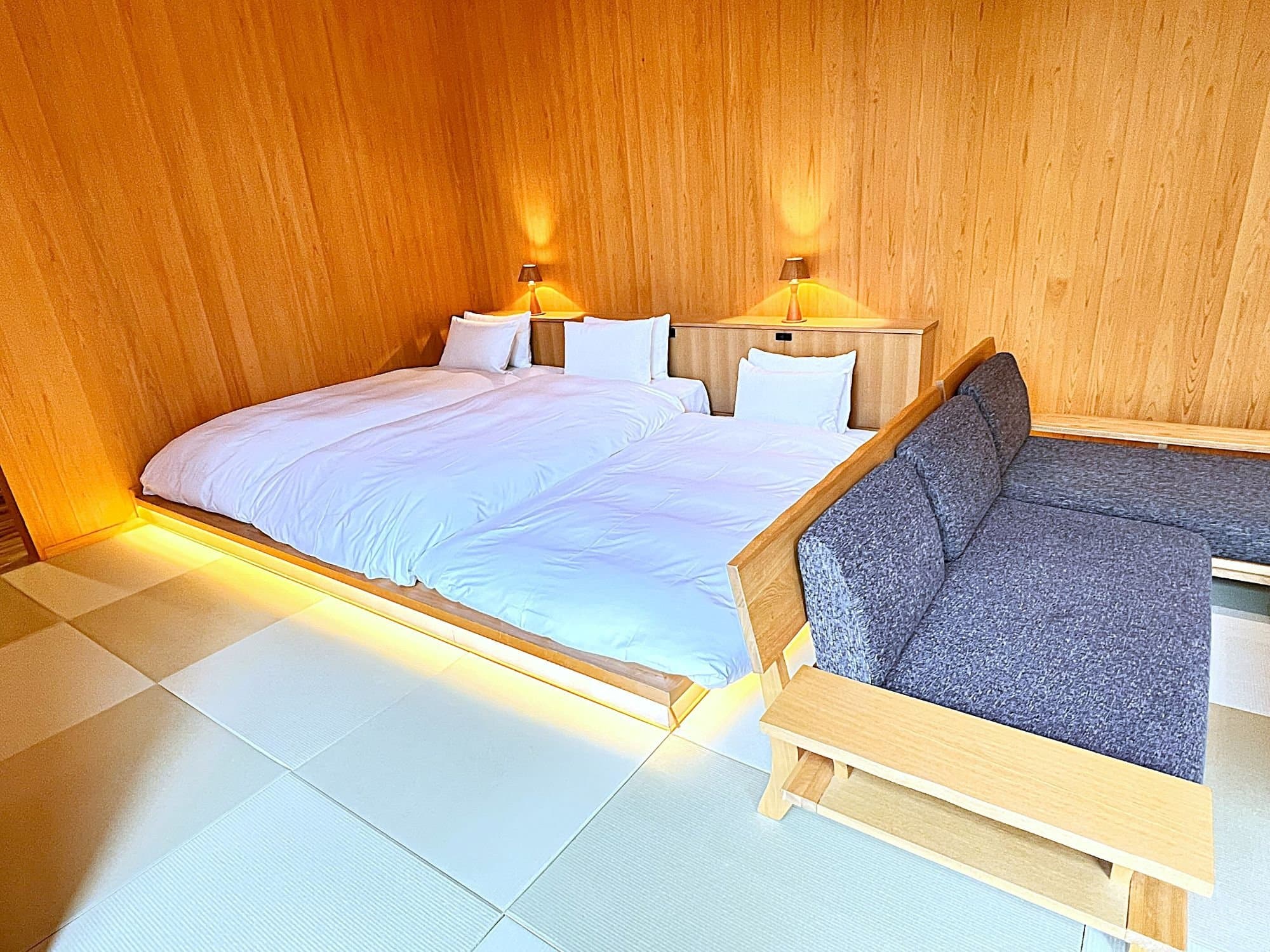 Guest bedroom with twin beds, sofa and warm indirect lighting over tatami flooring at Yamanote Bettei Hagakure