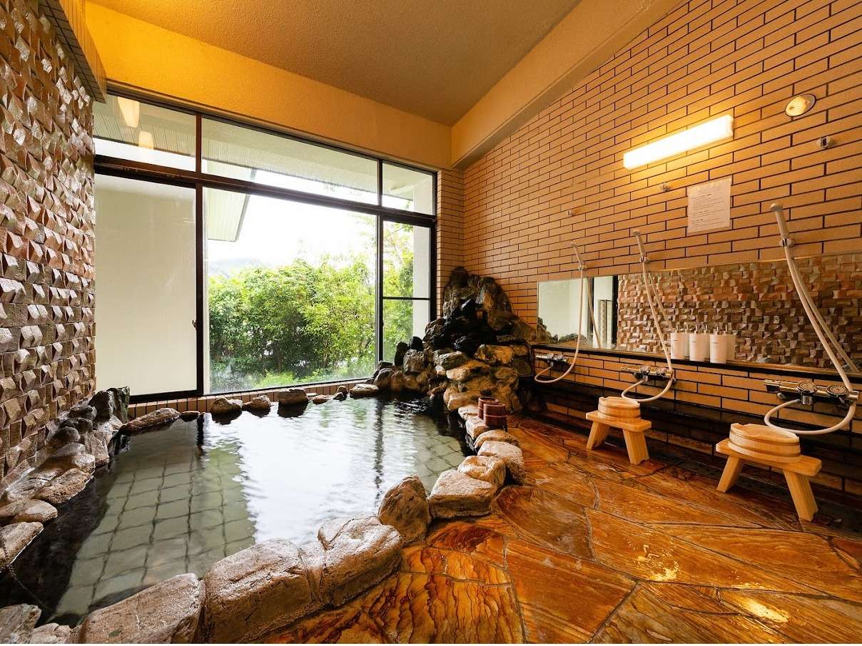 Indoor public hot-spring bath at Bisei Yufuin with stone pool, brick walls and washing stations
