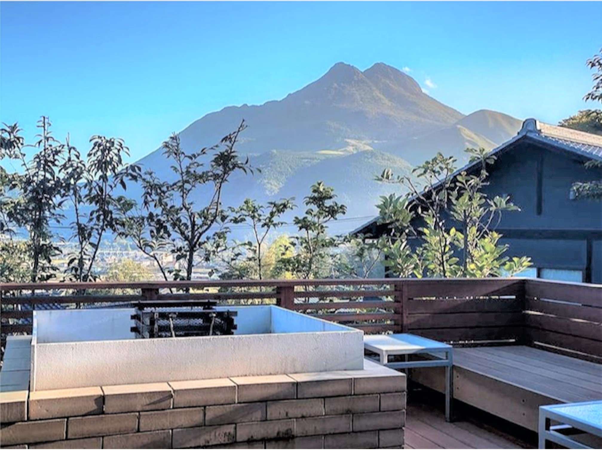 Wooden terrace at Bisei Yufuin overlooking Mount Yufu under a clear blue sky in Yufuin