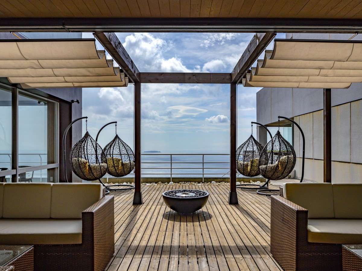 Rooftop lounge with hanging chairs and an open sea view over Atami at ISHINOYA Atami