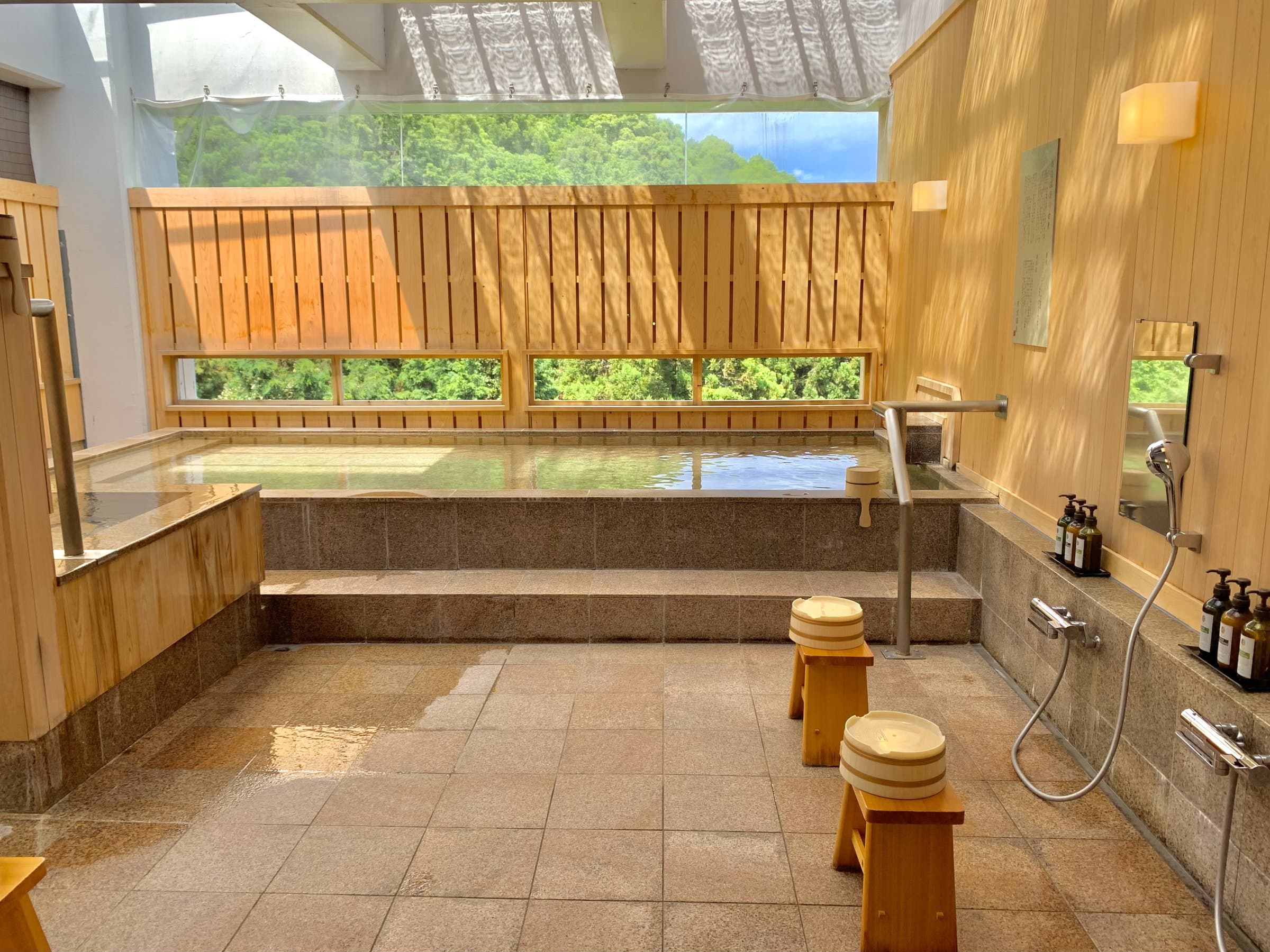 Indoor hot-spring bath with stone floor and forest view through wide windows at ISHINOYA Atami