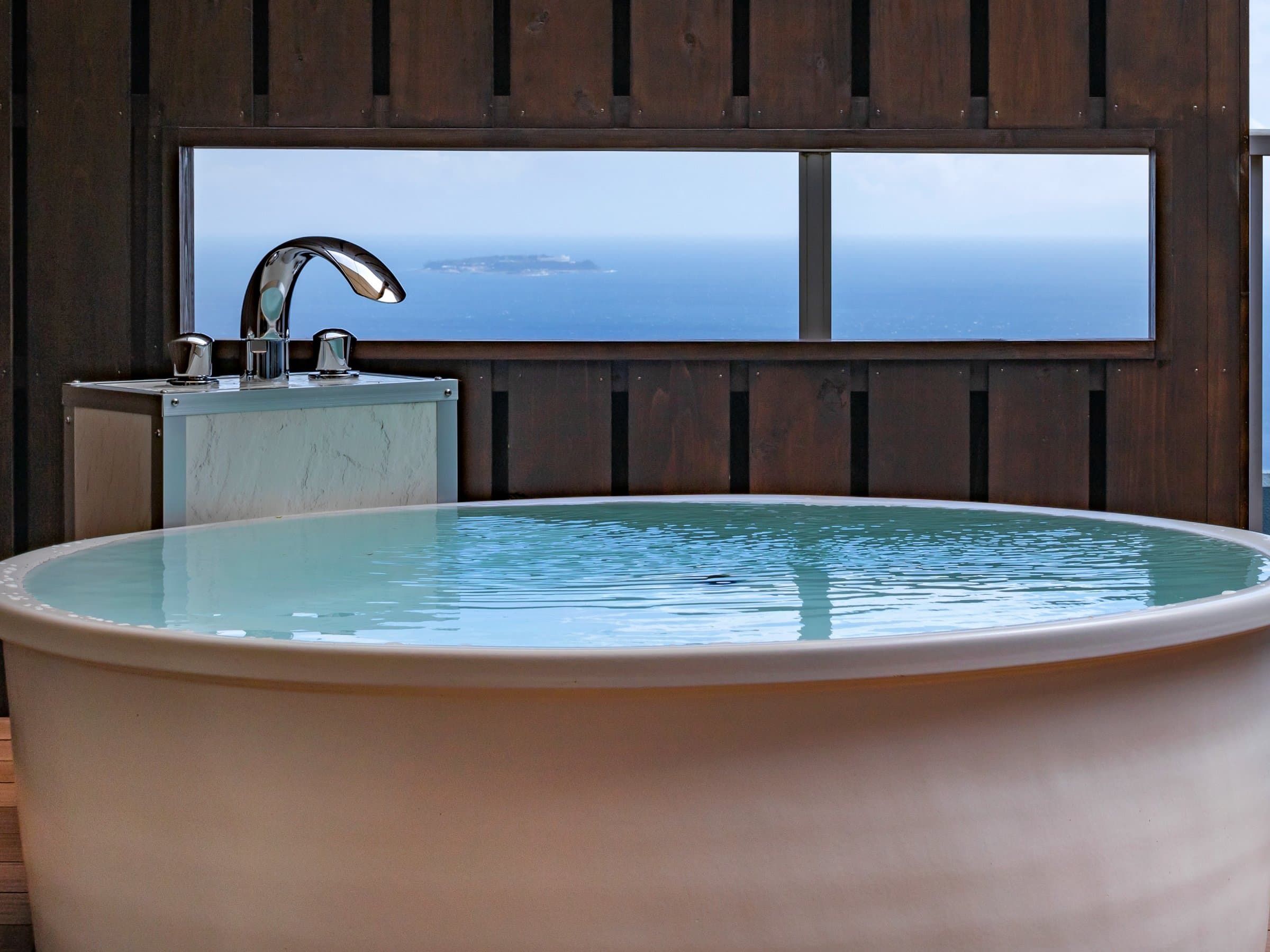 Round in-room bath framing an ocean and island view over Sagami Bay at ISHINOYA Atami