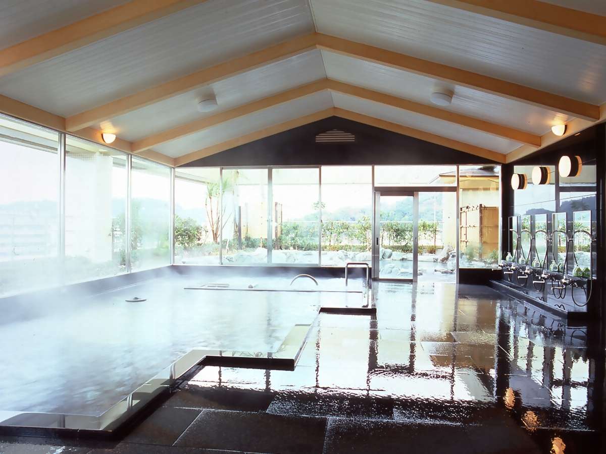 Spacious indoor public bath with steaming hot spring water, vaulted wooden ceiling and large garden-view windows