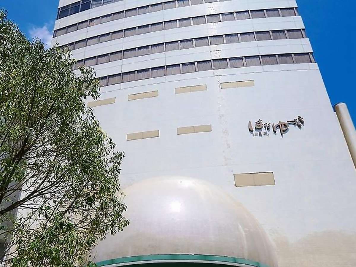Full exterior of the Hotel Hanayuzuki tower with rounded dome entrance under blue sky in Dogo Onsen, Matsuyama
