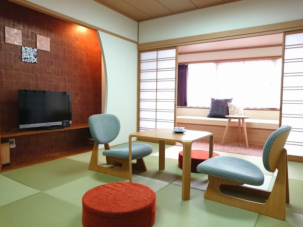 Japanese-style tatami guest room with low chairs, low table and a shoji-screened window bench at Dogo Onsen Hanayuzuki