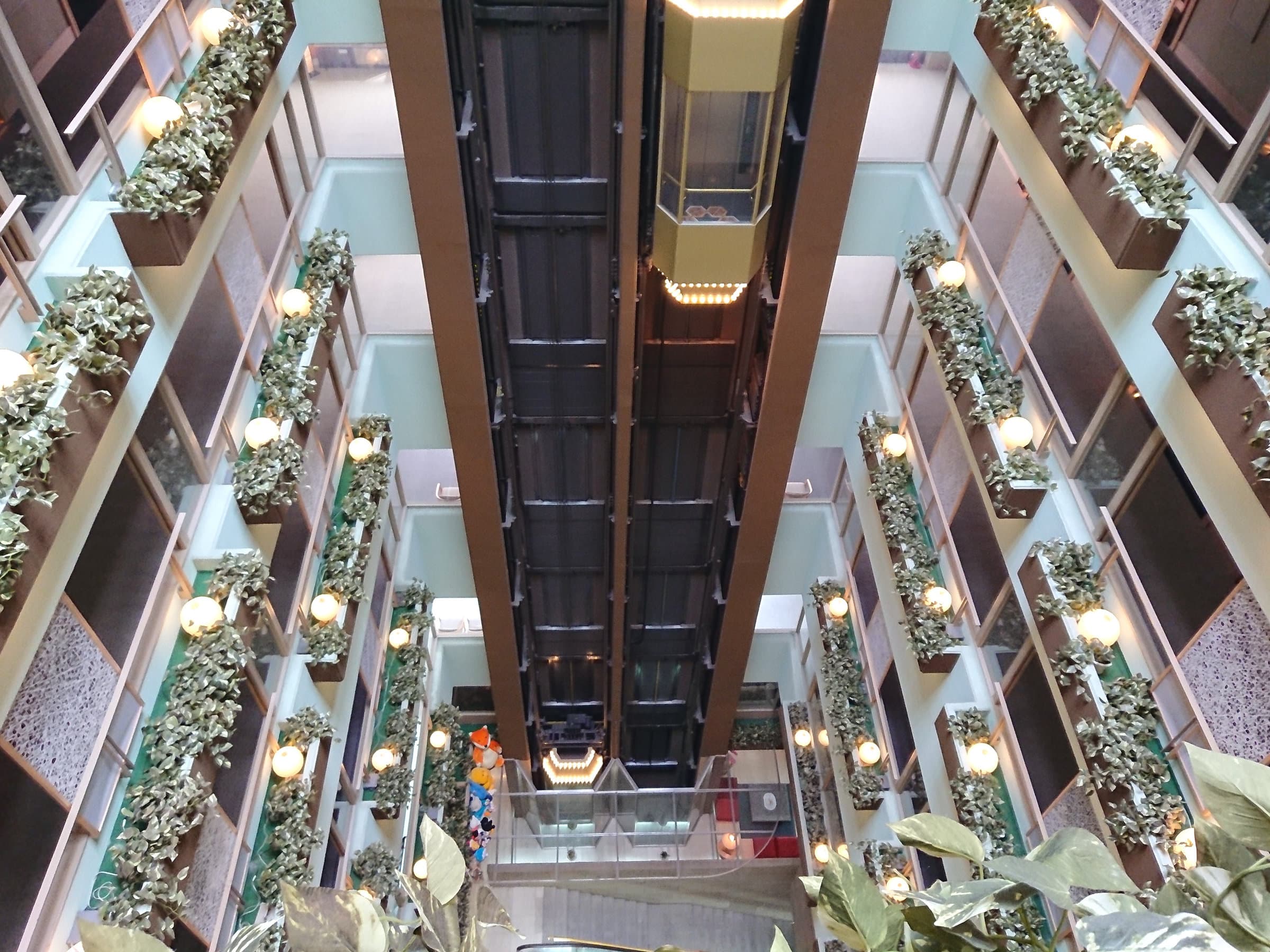 Multi-floor interior atrium with glass elevator and cascading greenery along the corridors at Dogo Onsen Hanayuzuki