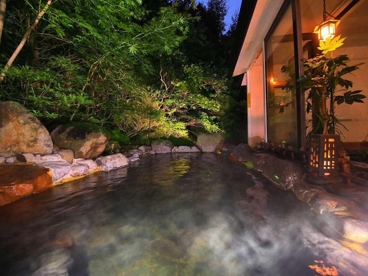 Outdoor onsen bath steaming at night beside a lit lantern and greenery at Mori no Yu Sanseikan in Karurusu Onsen