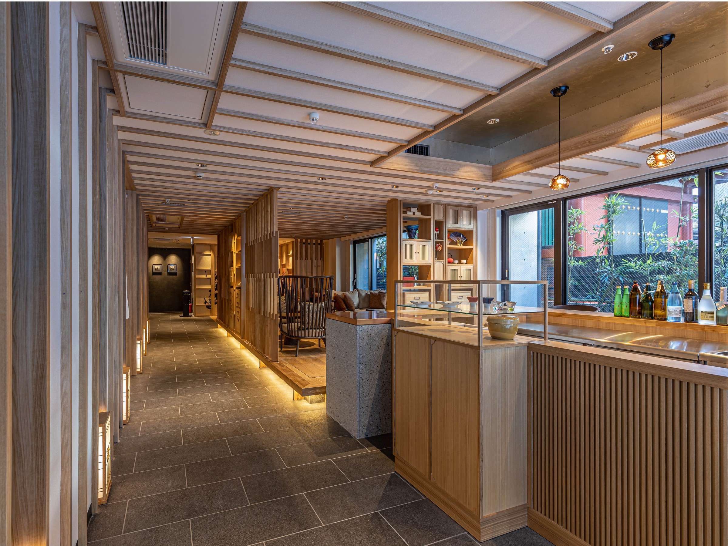Wood-toned guest lounge and sake bar counter with lantern pendants and large garden window