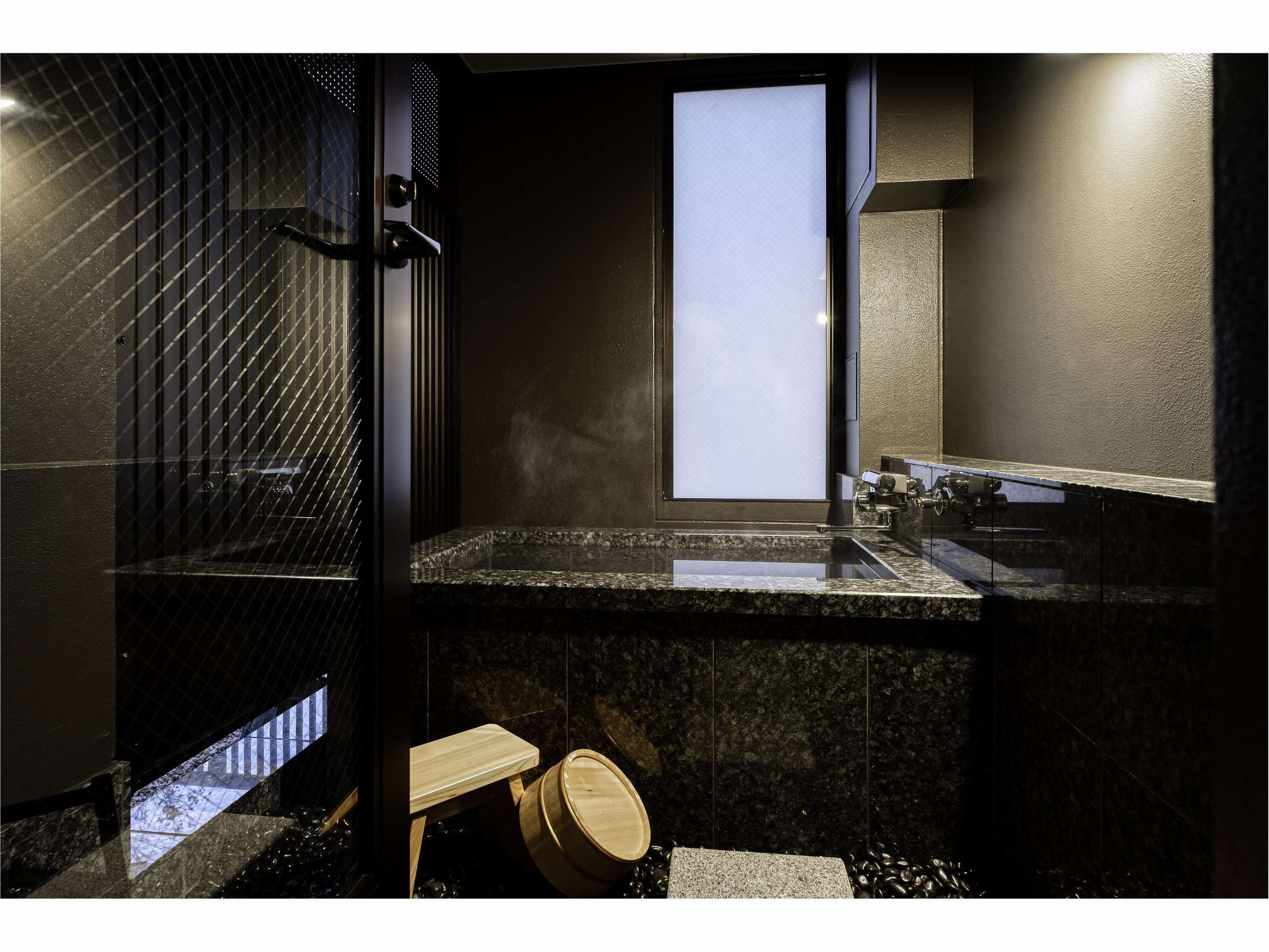 Private in-room stone bath in dark granite with rising steam, wooden stool and pail