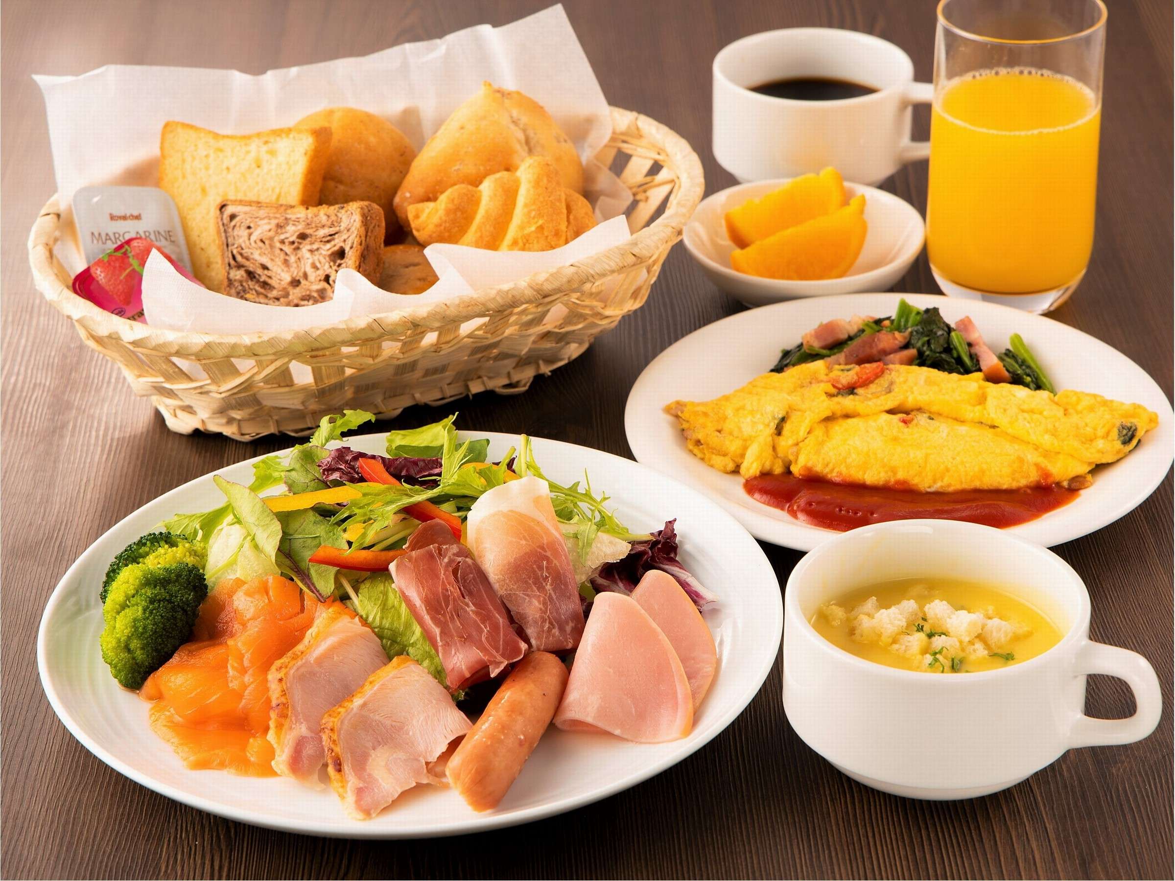 Western breakfast plate of omelette, ham, salad, bread basket, soup, coffee and orange juice