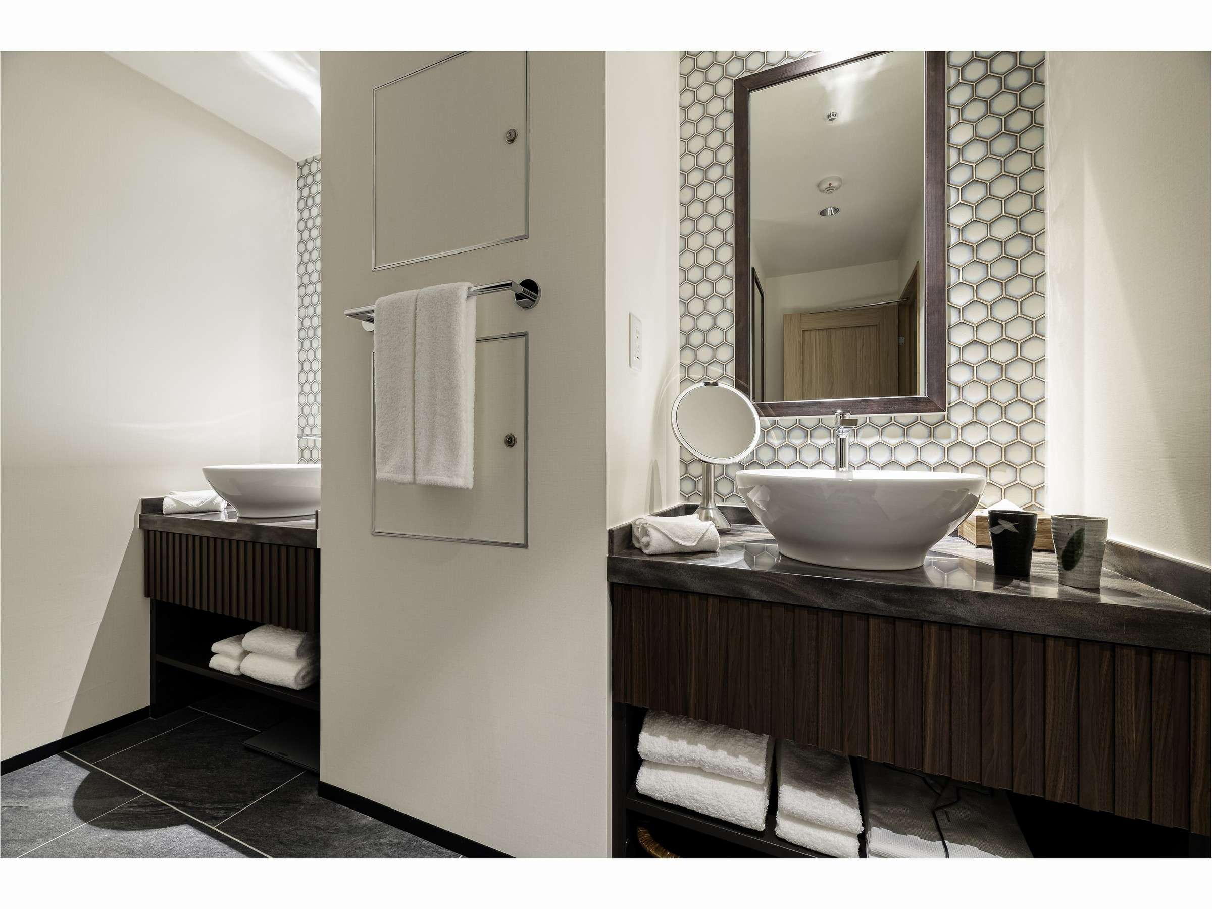 Guest room vanity with twin vessel basins, hexagonal tile wall, framed mirror and folded towels