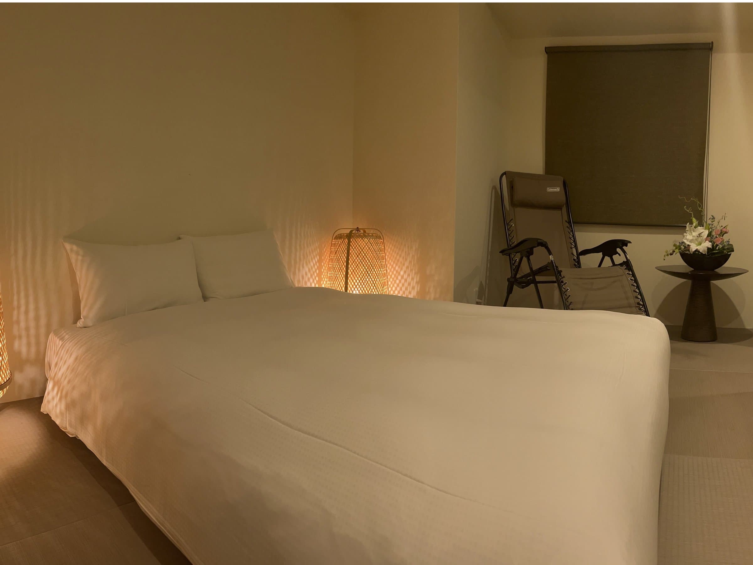 Modern guest room with a low double bed, woven lantern lamp and relaxer chairs in warm lighting