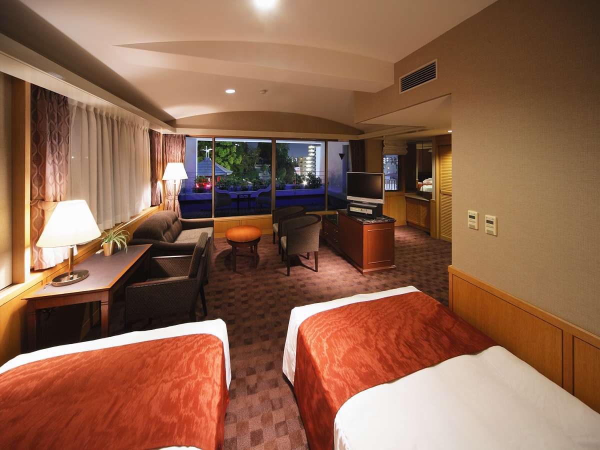 Spacious deluxe twin room with sitting area and evening city view at Hotel Patio Dogo