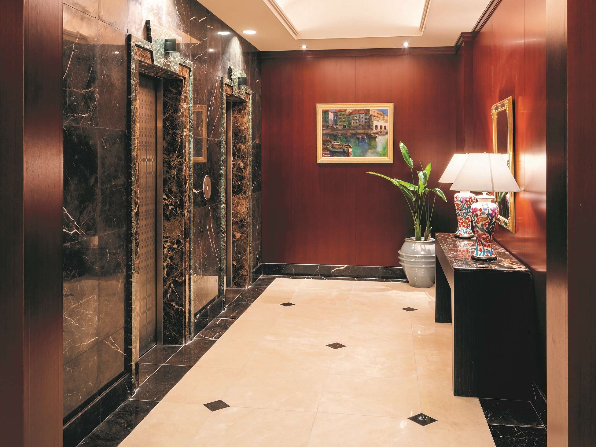 Marble and wood-panelled elevator hall with framed art and lamp at Hotel Patio Dogo