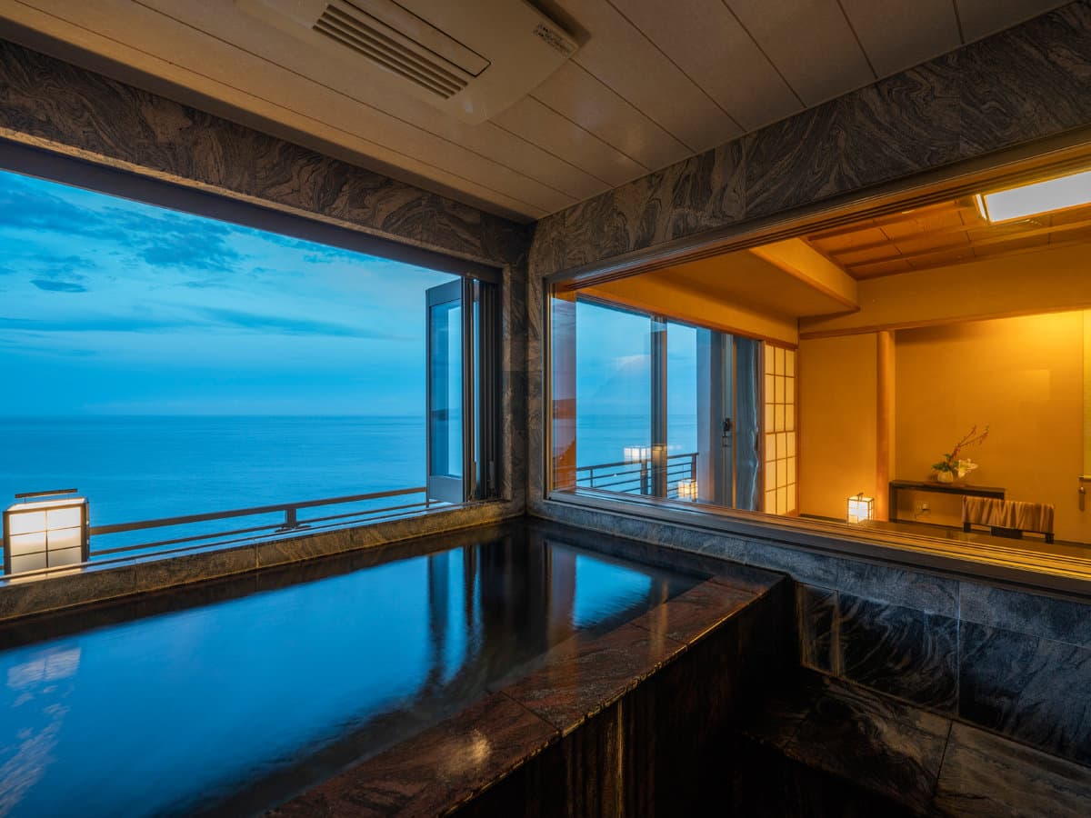 Private guest-room bath beside a tatami room with twilight ocean view at Kissho Caren