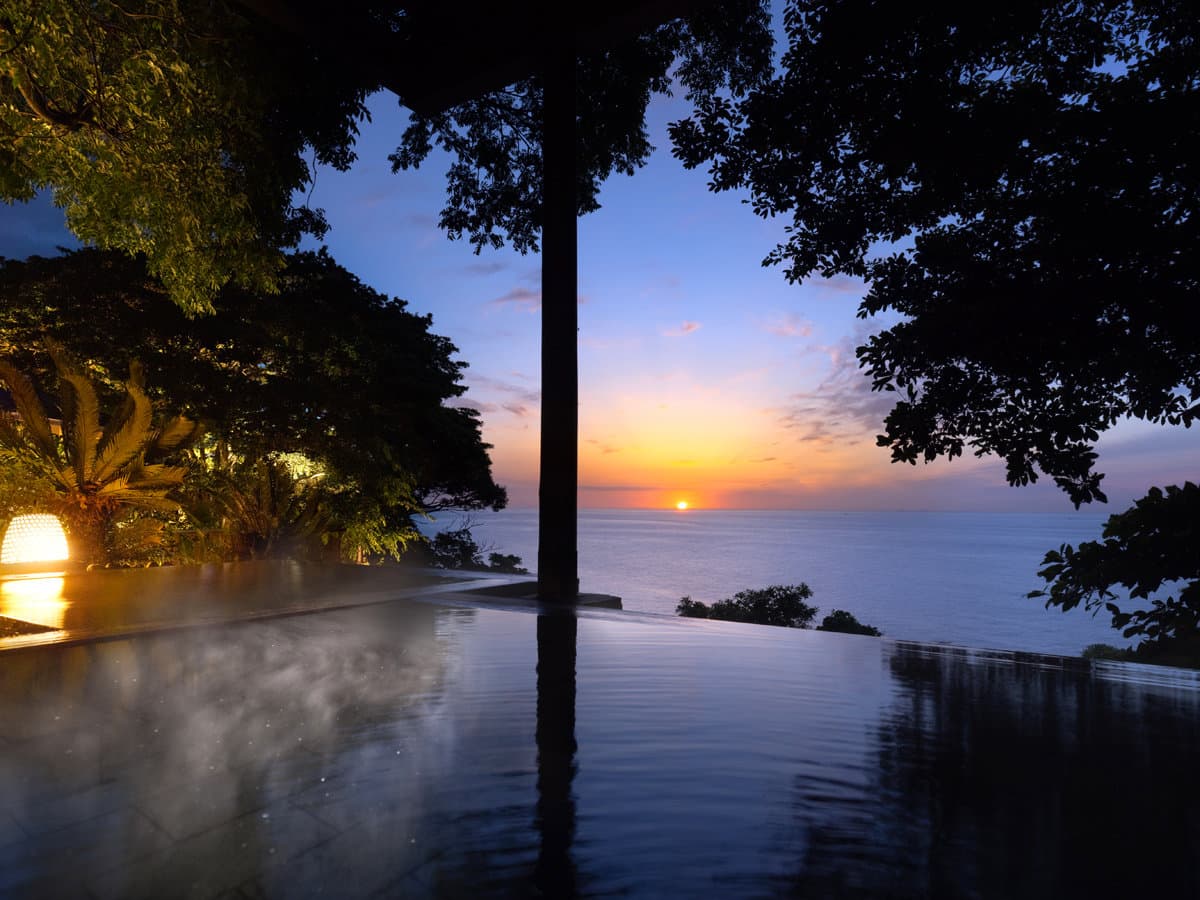 Steaming open-air hot spring bath at Kissho Caren framing an ocean sunset over the Izu coast
