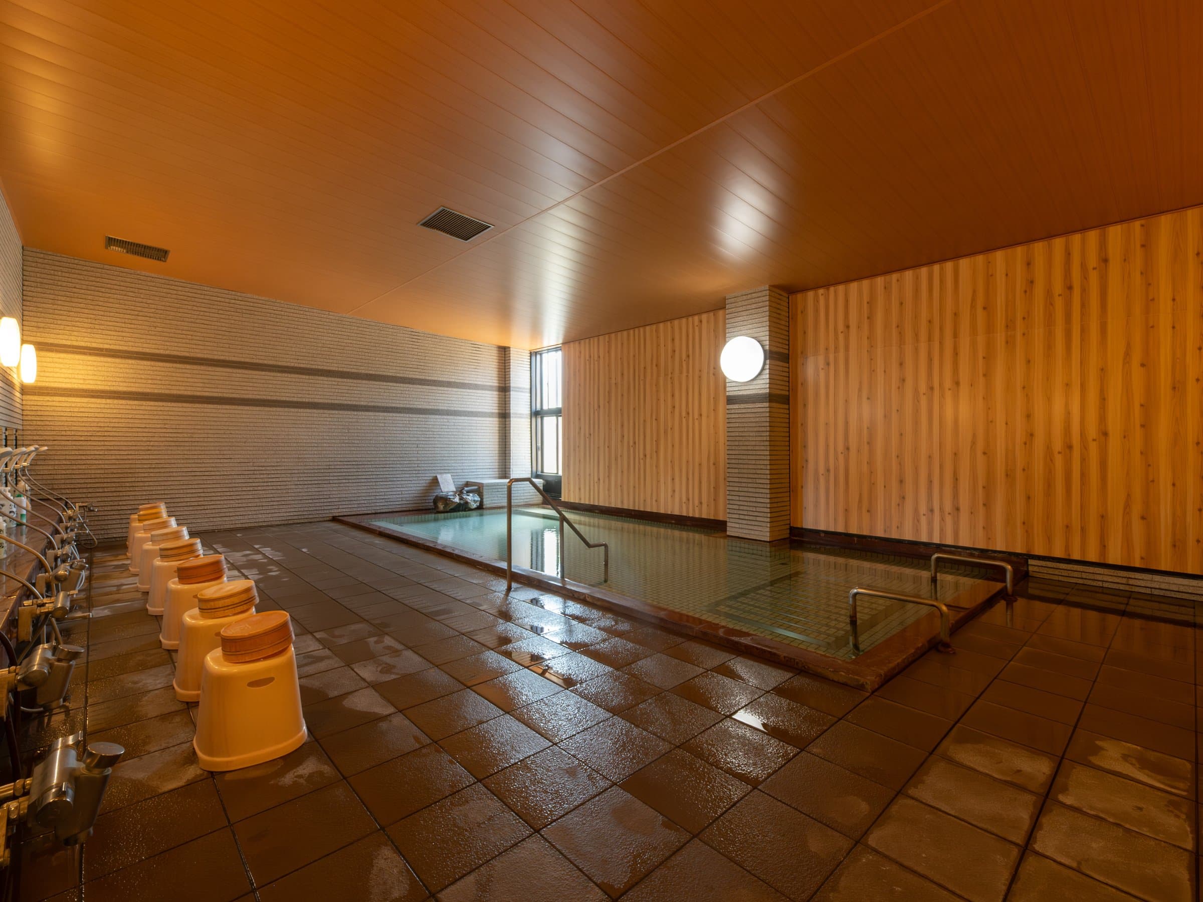 Spacious indoor hot-spring bath with wood ceiling and washing stations at Hamazuru, Wakura Onsen