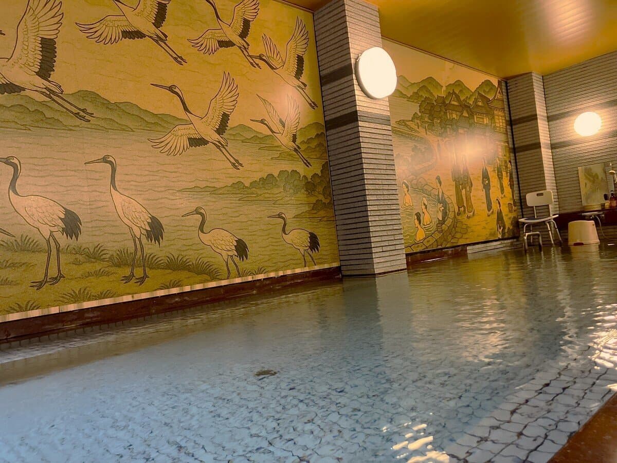 Indoor onsen bath at Hamazuru with a painted crane mural reflected in the steaming water