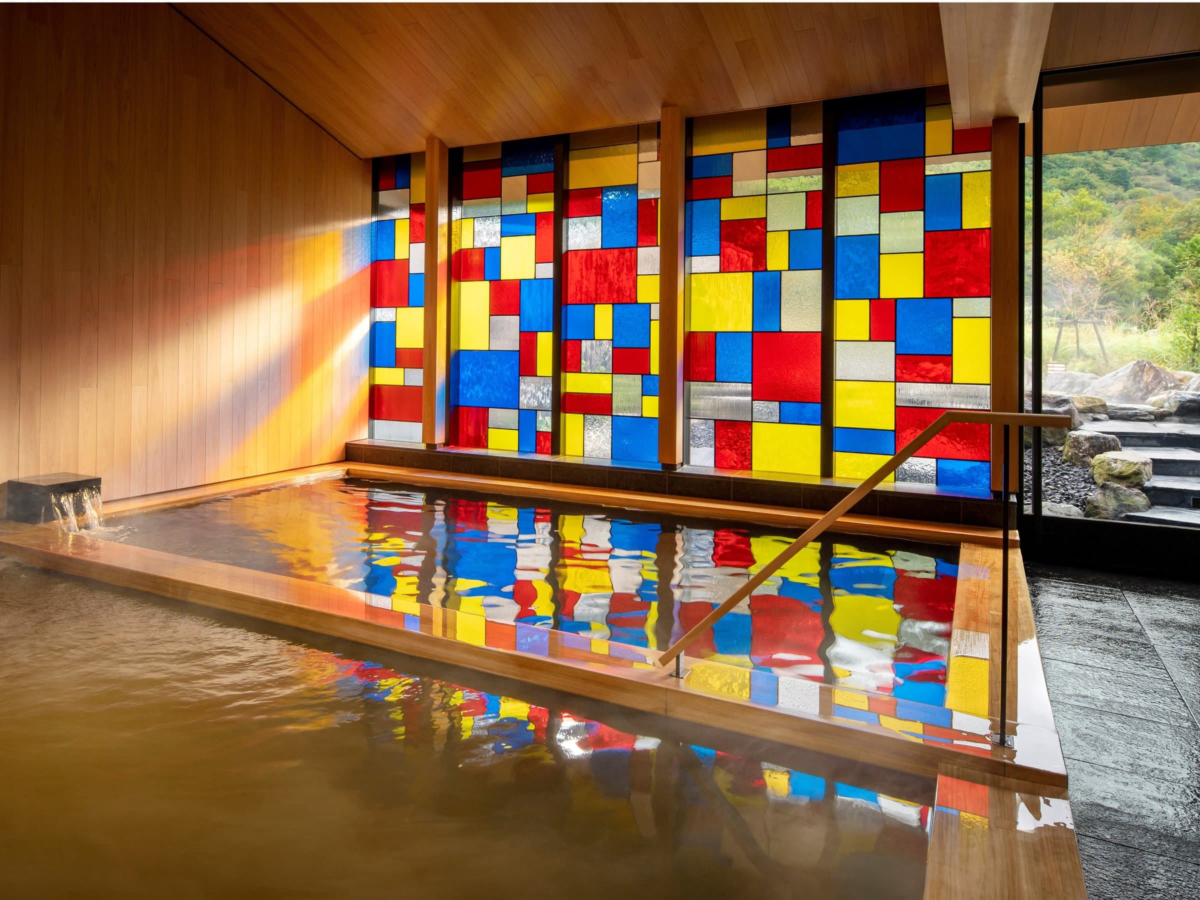 Indoor hot-spring bath at KAI Unzen with a wall of colorful Vidro stained glass casting reflections on the steaming water