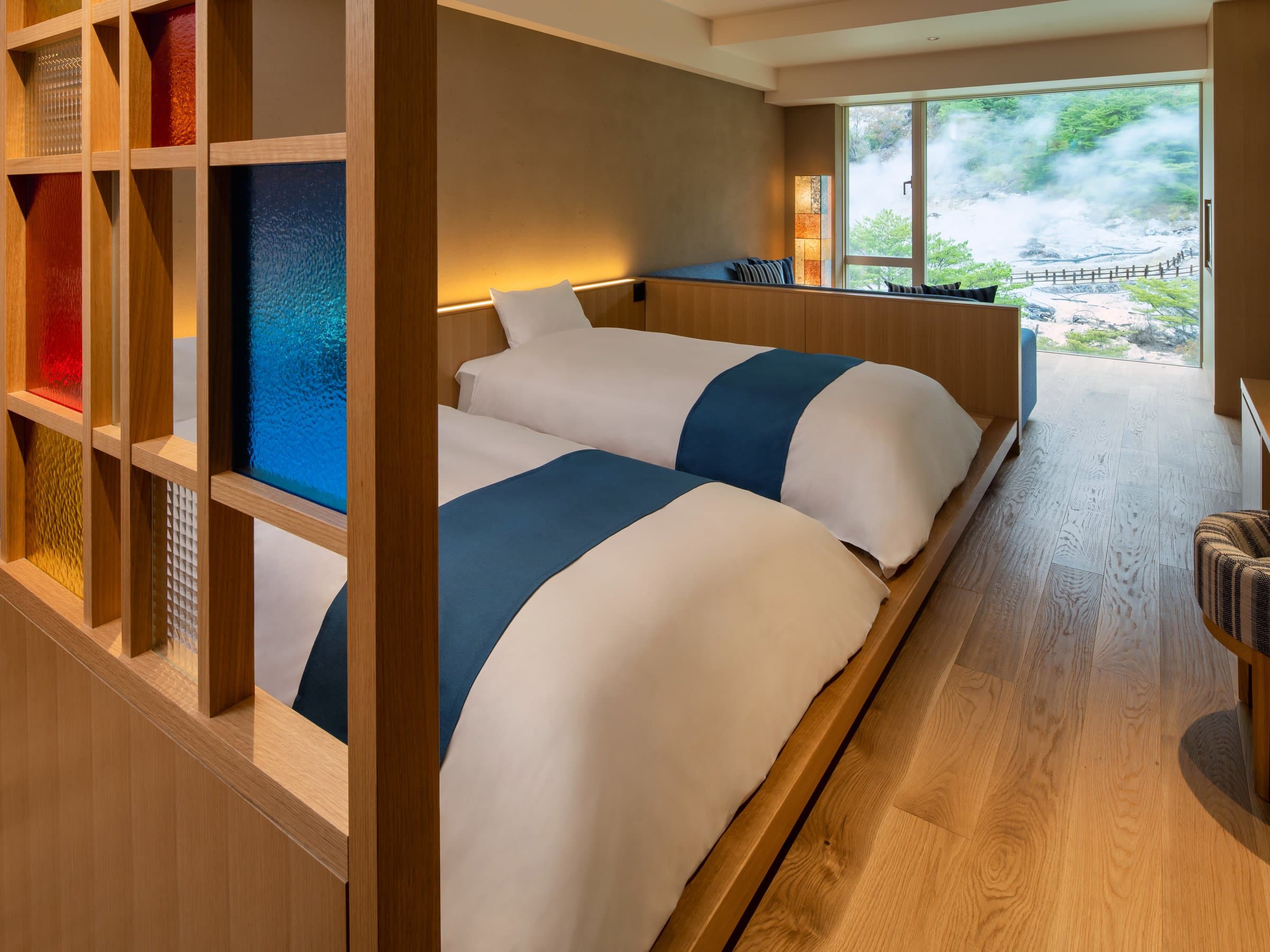 Twin-bed guest room at KAI Unzen with wooden partition of colored glass and a window overlooking the steaming Unzen hot-spring grounds