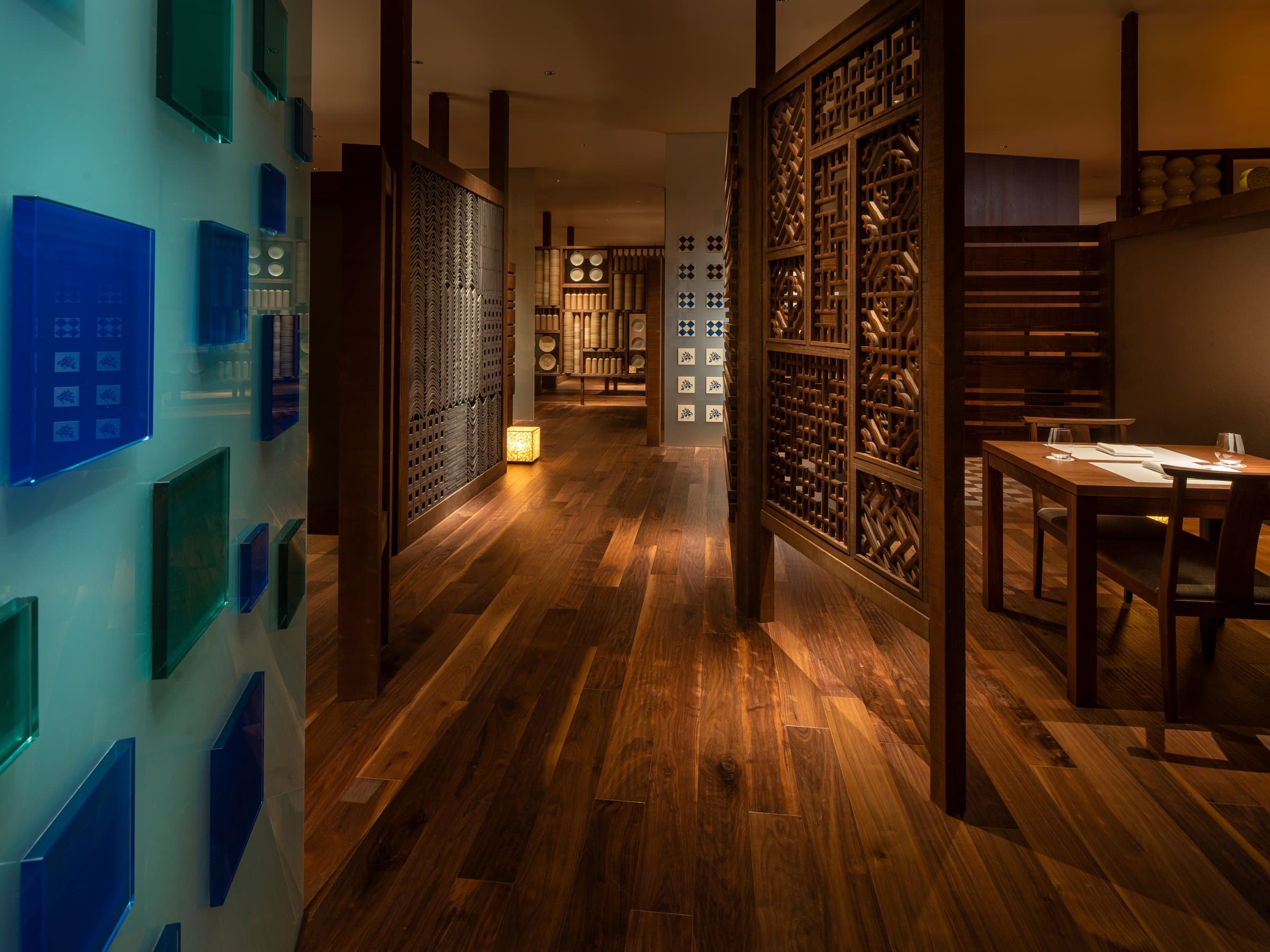 Dining area corridor at KAI Unzen with walnut flooring, carved wood screens and a wall of colored Vidro glass tiles