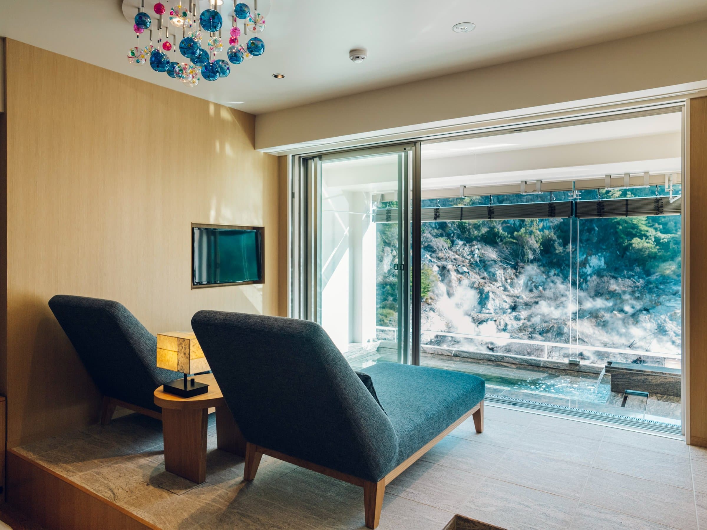 Guest room lounge area at KAI Unzen with reclining chairs facing a picture window onto the steaming Unzen Jigoku hell valley