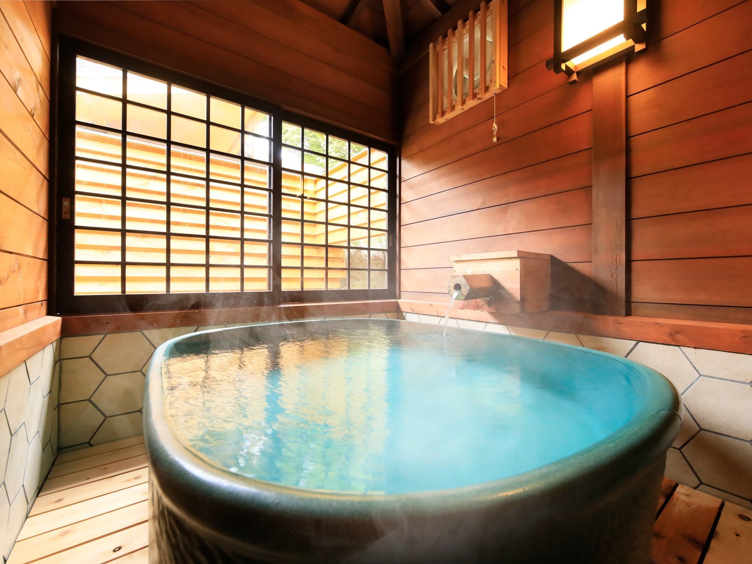 Private rental bath at Yuyado Miyuki Honkan in Kusatsu with a black oval tub of steaming pale-blue spring water in a cedar-walled room with a shoji window