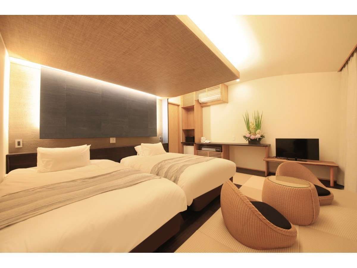 Warm-toned twin guest room at Yuyado Miyuki Honkan with cream bedding, an ikebana arrangement and rattan chairs on tatami