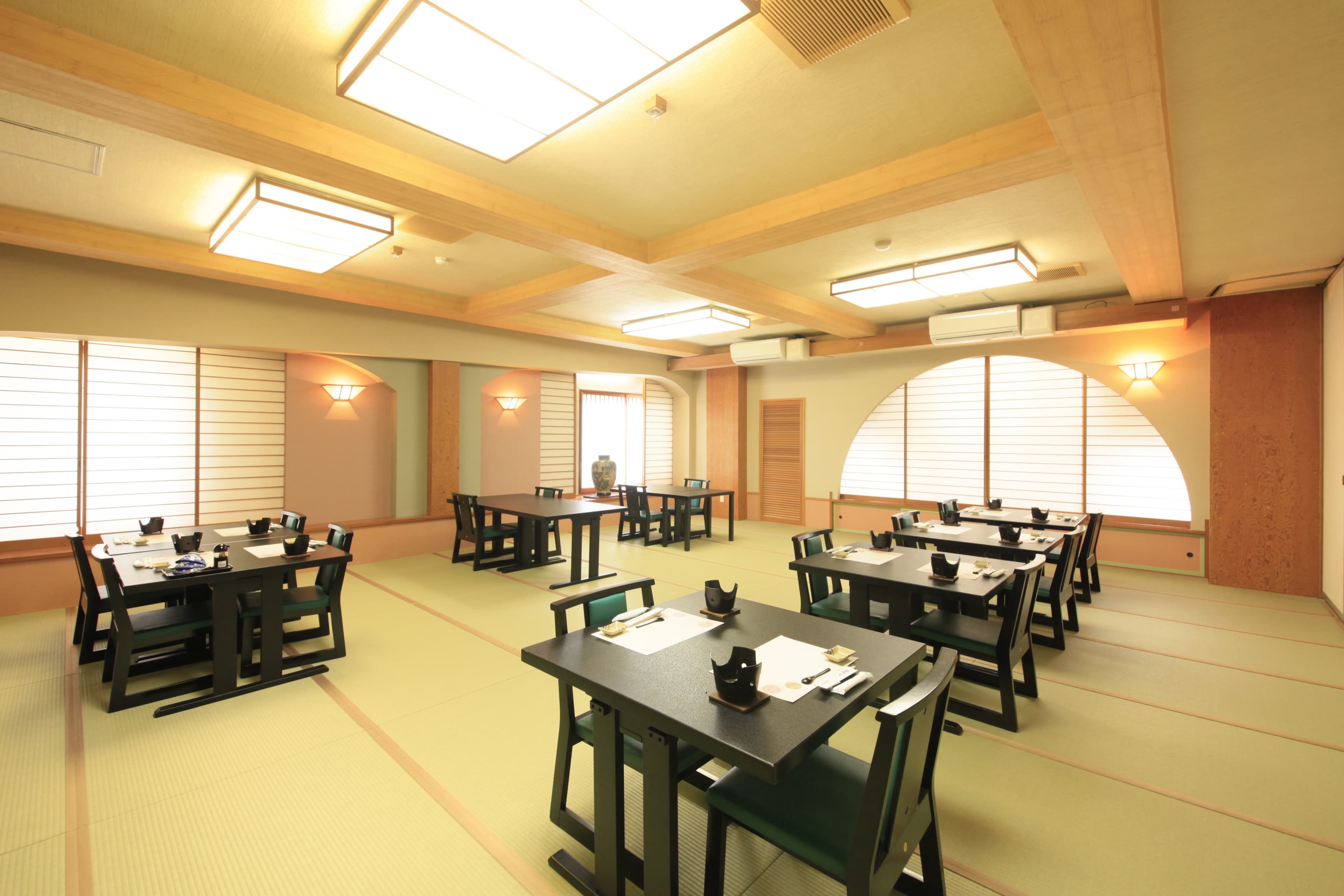 Tatami dining hall at Yuyado Miyuki Honkan with rows of black tables and chairs beneath square paper lanterns