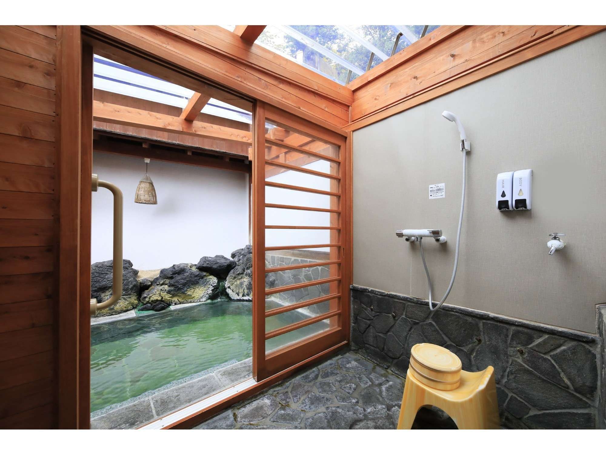 Private rental bath at Yuyado Miyuki Honkan with a lava-rock-edged stone pool of green thermal water under a glass roof
