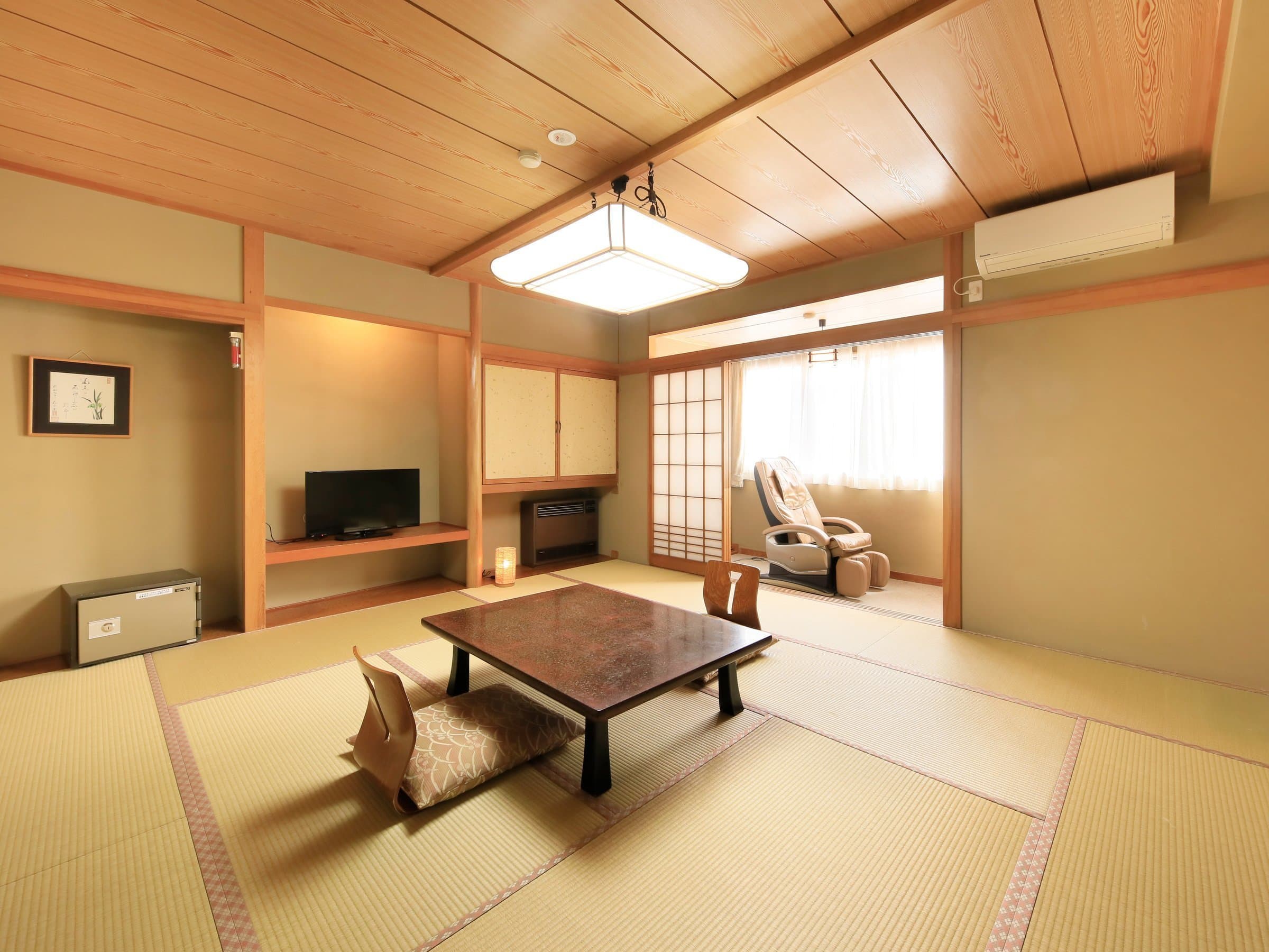 Spacious tatami guest room at Yuyado Miyuki Honkan with a low lacquered table, floor cushions and a massage chair by the window
