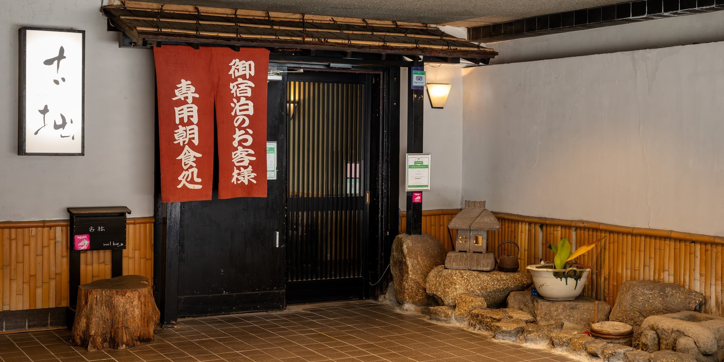 Restaurant entrance framed by a red noren curtain, stone lantern and small rock garden at Hotel Edoya, Tokyo