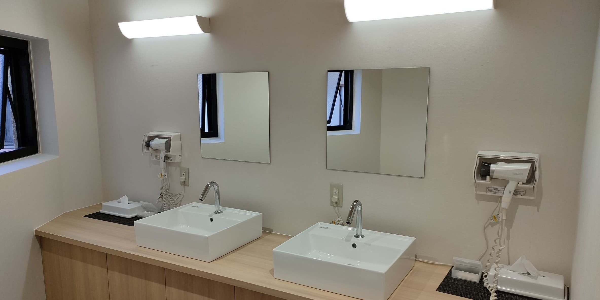 Bright powder room with twin vanity sinks, mirrors and hair dryers beside the bath at Hotel Edoya, Tokyo