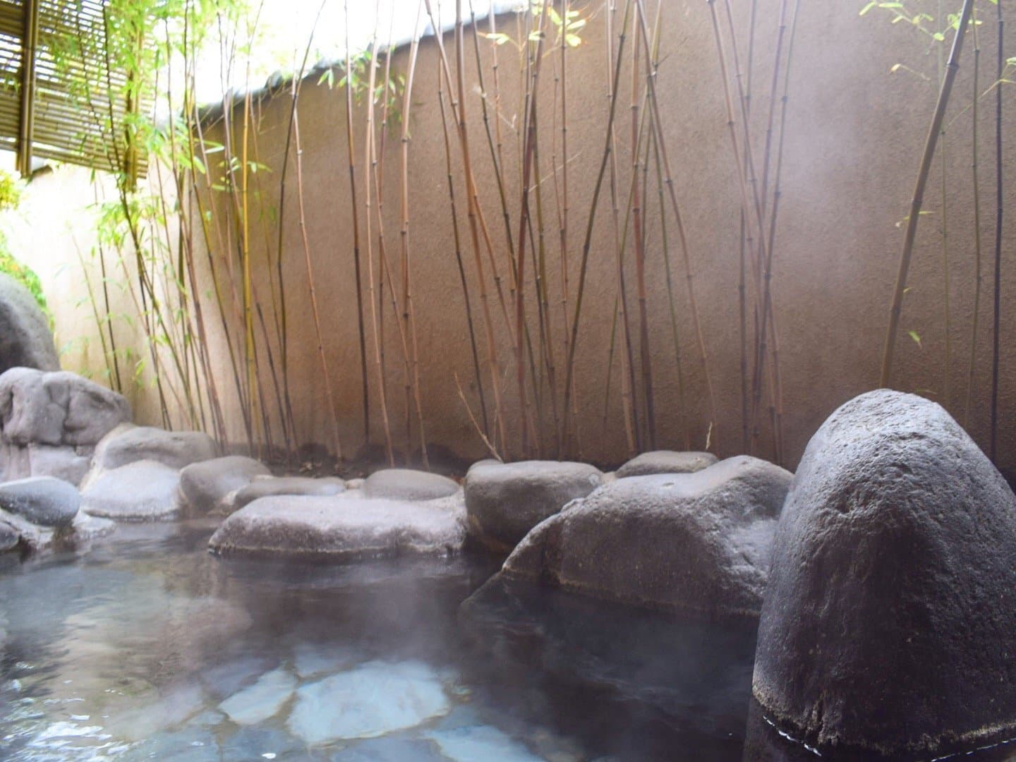 Outdoor rotenburo stone bath at Soraichi surrounded by bamboo with rising steam at Akiu Onsen