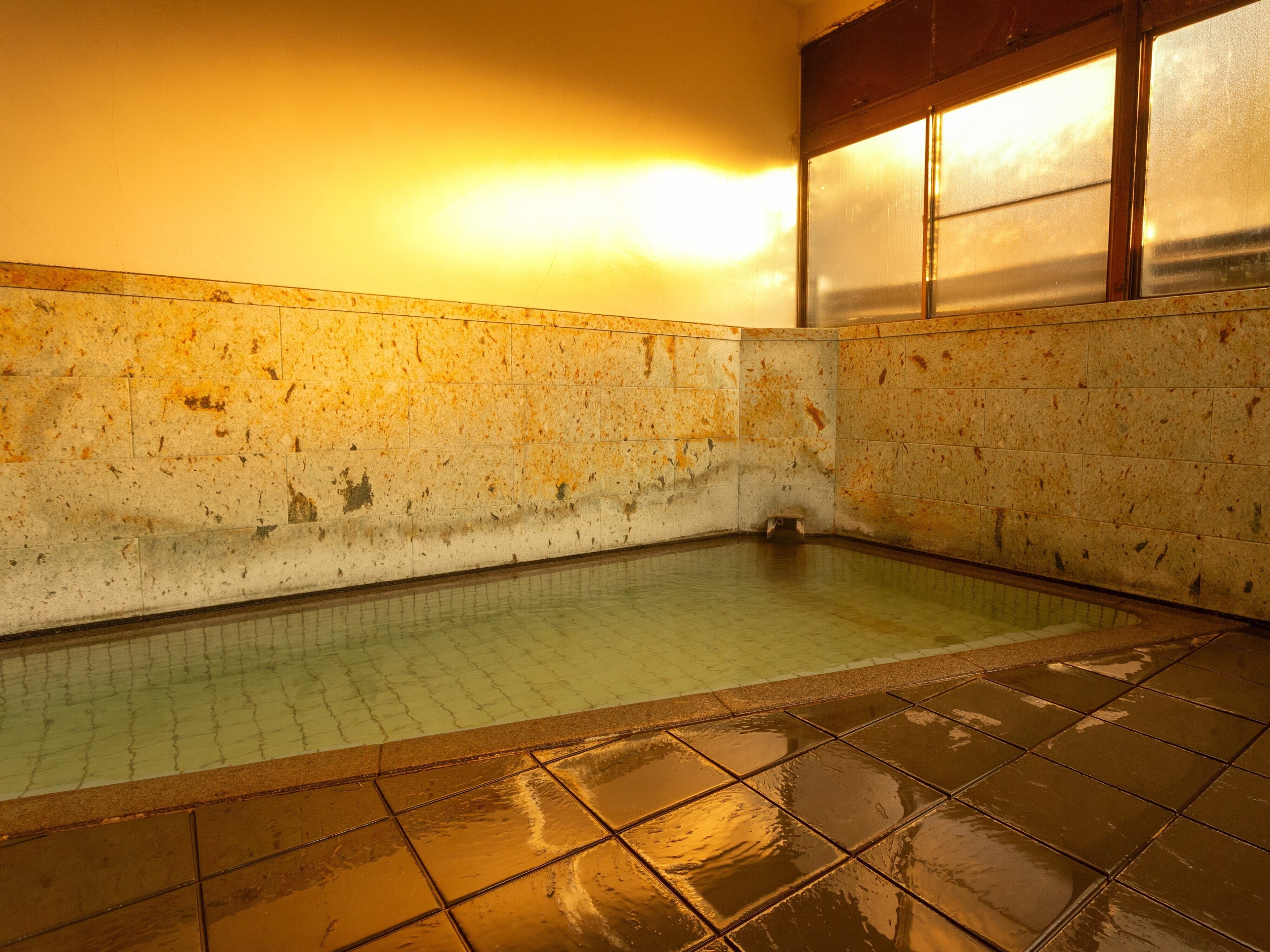 Indoor onsen bath at Soraichi with stone-tiled walls and green mineral-rich thermal water