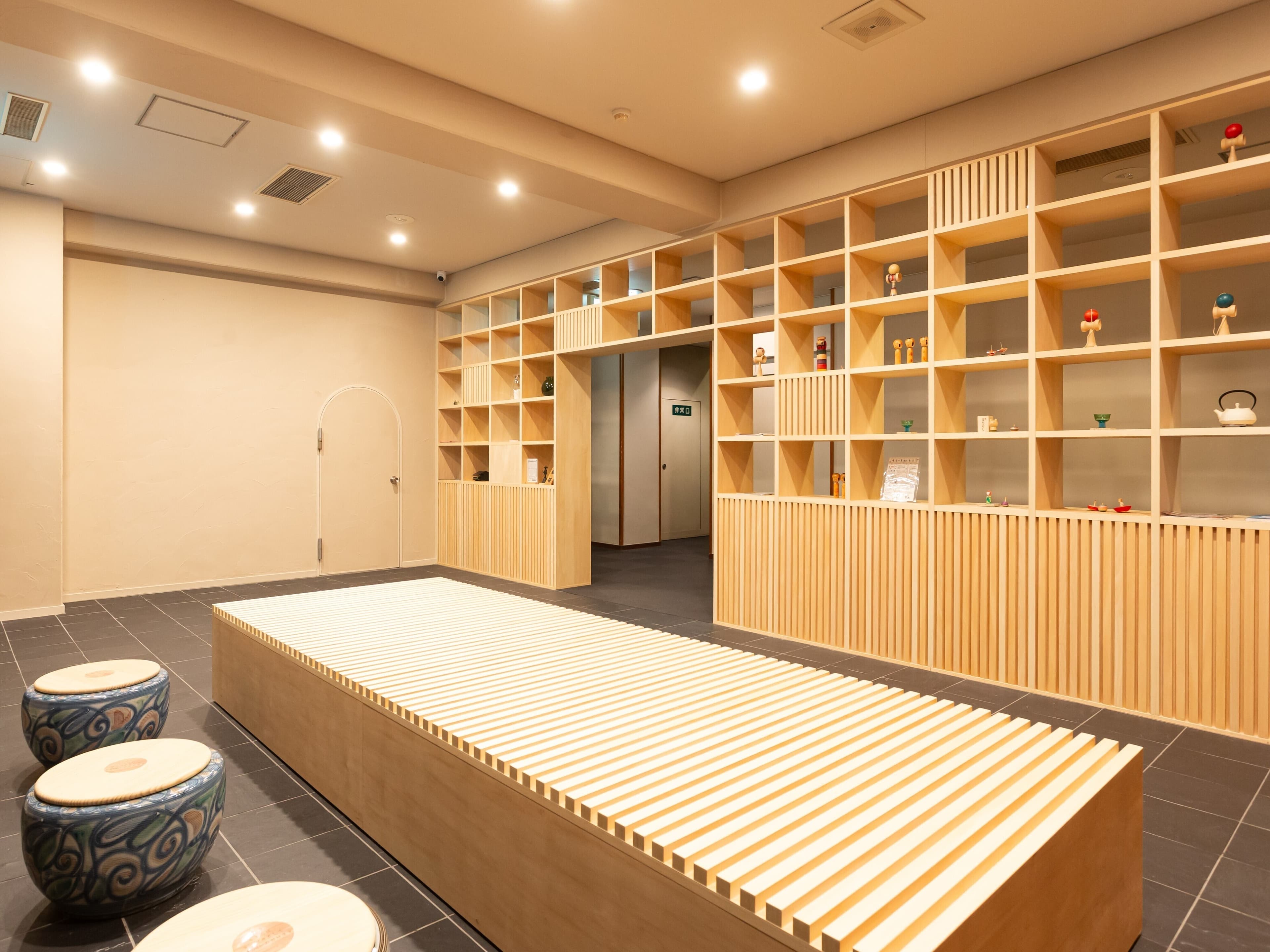 Relaxation lounge at Soraichi with wooden bench seating, kokeshi-doll shelving and tile floor