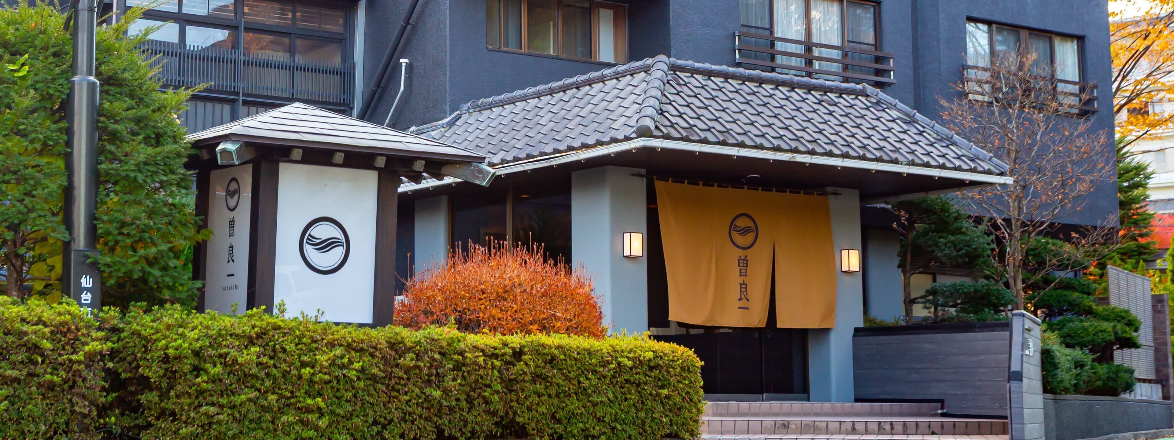 Soraichi ryokan entrance and tiled-roof facade with indigo noren curtains at Akiu Onsen