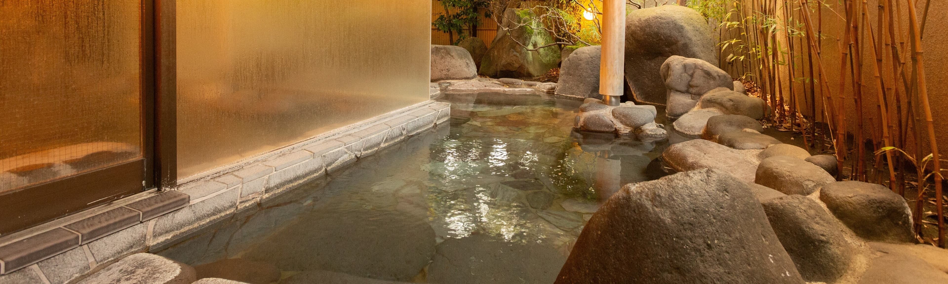 Evening view of Soraichi's open-air hot spring bath framed by rocks and bamboo at Akiu Onsen