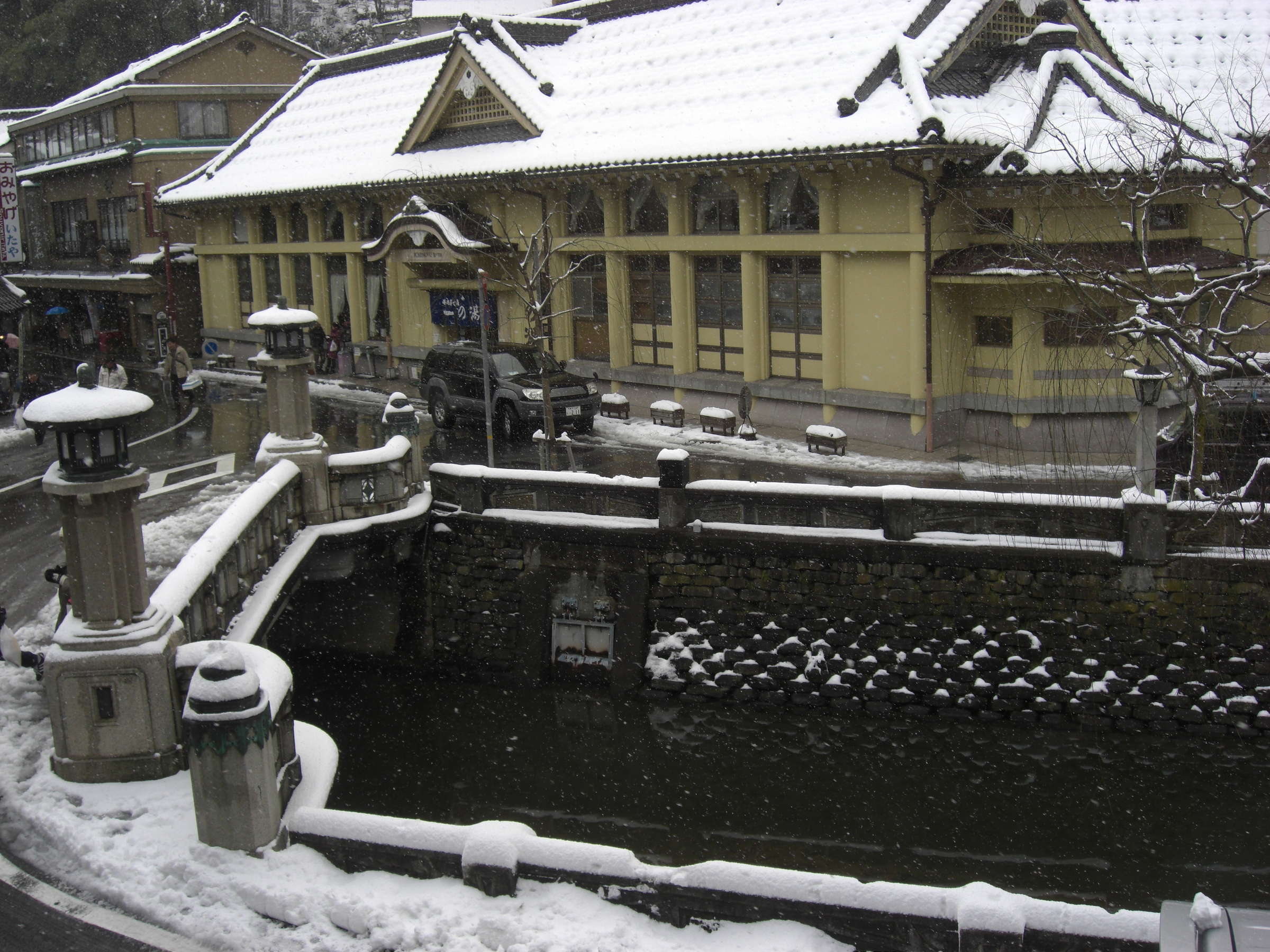 Snow-covered Kinosaki Onsen townscape with stone bridge and bathhouse near Matsuya