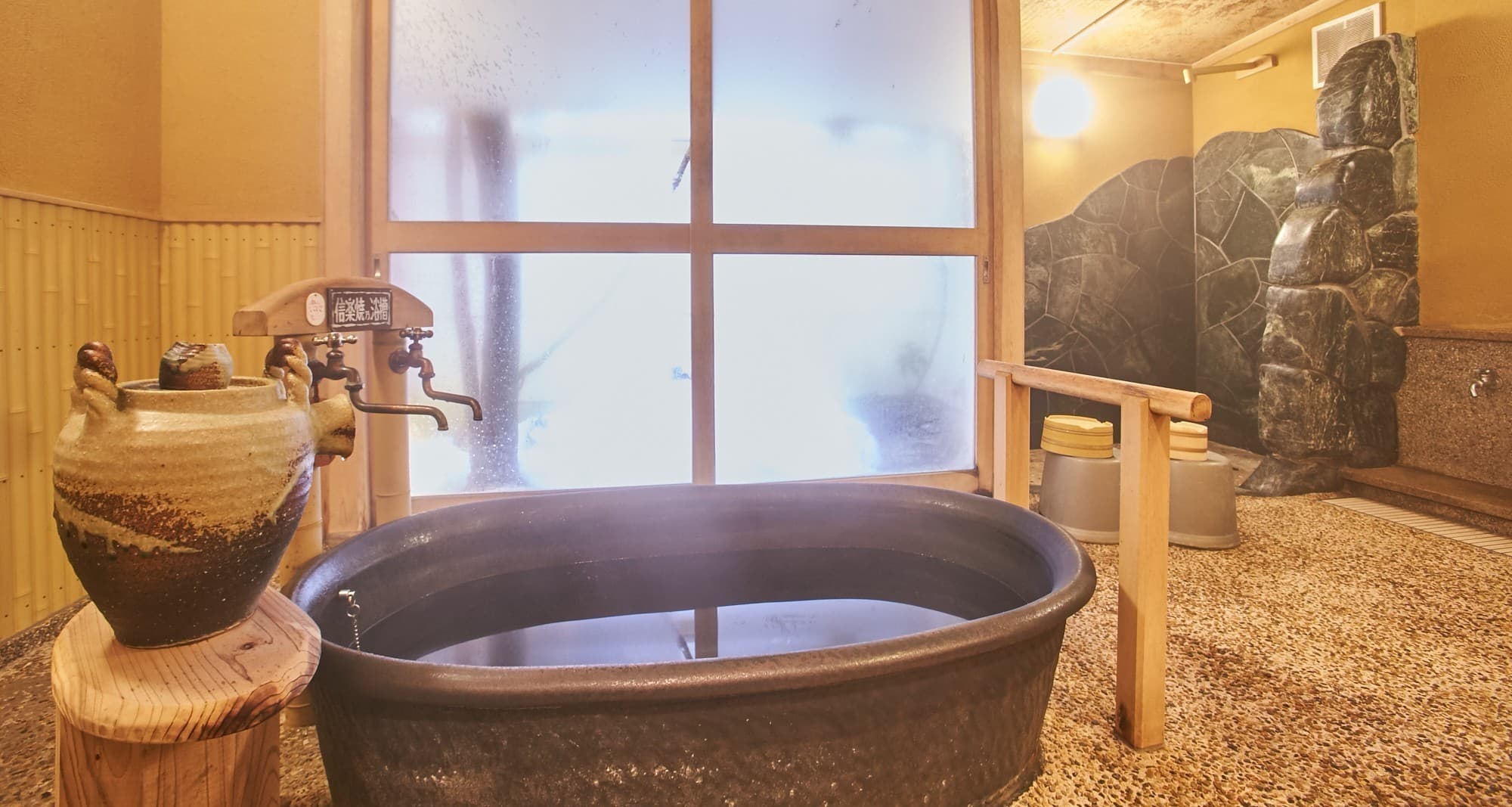 Cast-iron goemon soaking tub bath at Matsuya beside a stone wall and pebble floor