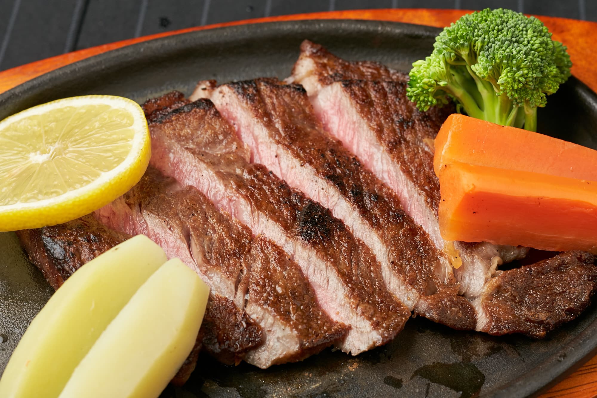 Seared sliced beef steak on a hot iron plate with vegetables at Matsuya