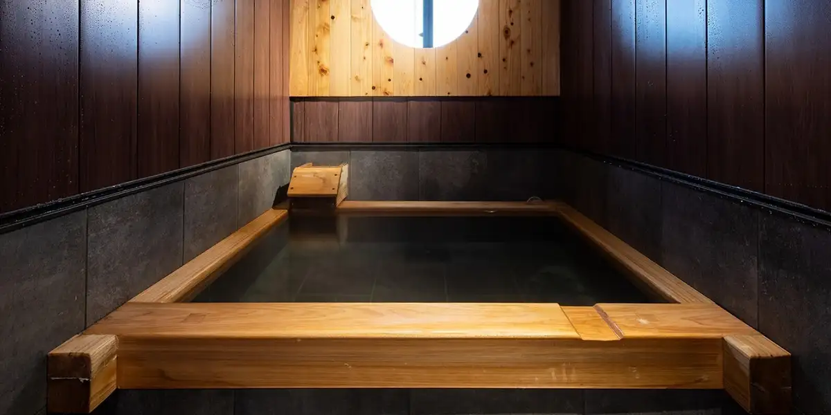 Private cypress-framed hot spring bath at Suehiroya Ryokan with a round window and dark slate surround