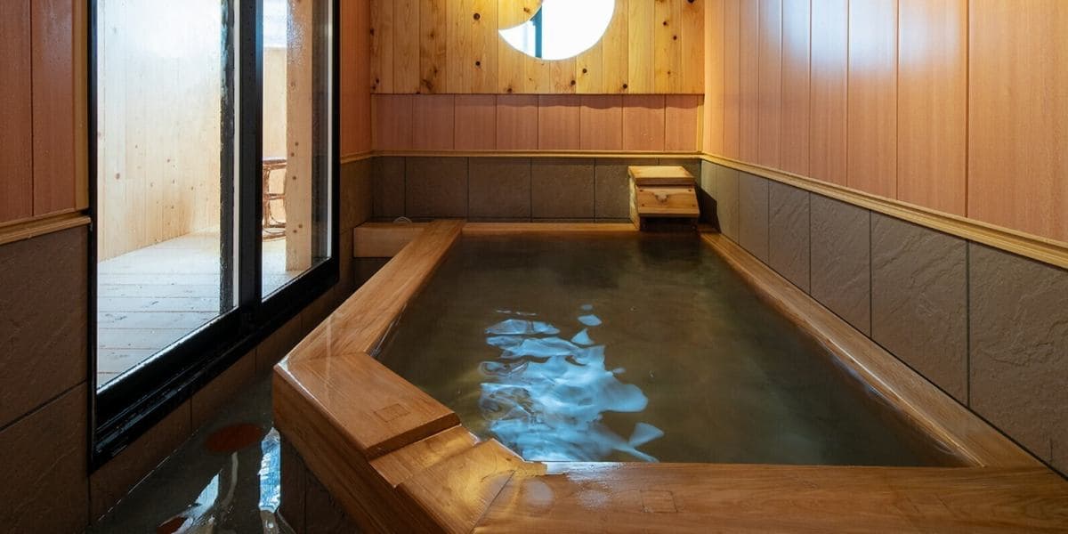 Private wooden hot spring bath at Suehiroya Ryokan with a round window and an adjoining changing space behind glass
