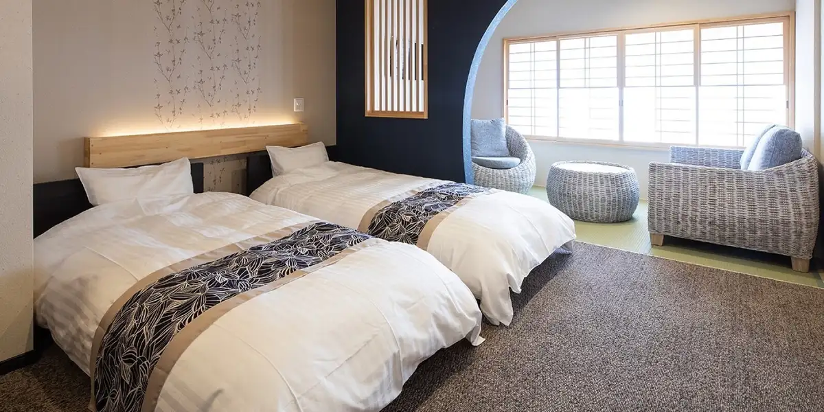Guest room at Suehiroya Ryokan with twin beds, an arched navy alcove and woven rattan chairs by the window