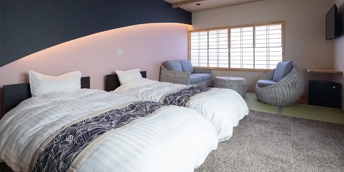 Guest room at Suehiroya Ryokan with twin beds against a curved pink and navy accent wall and rattan seating