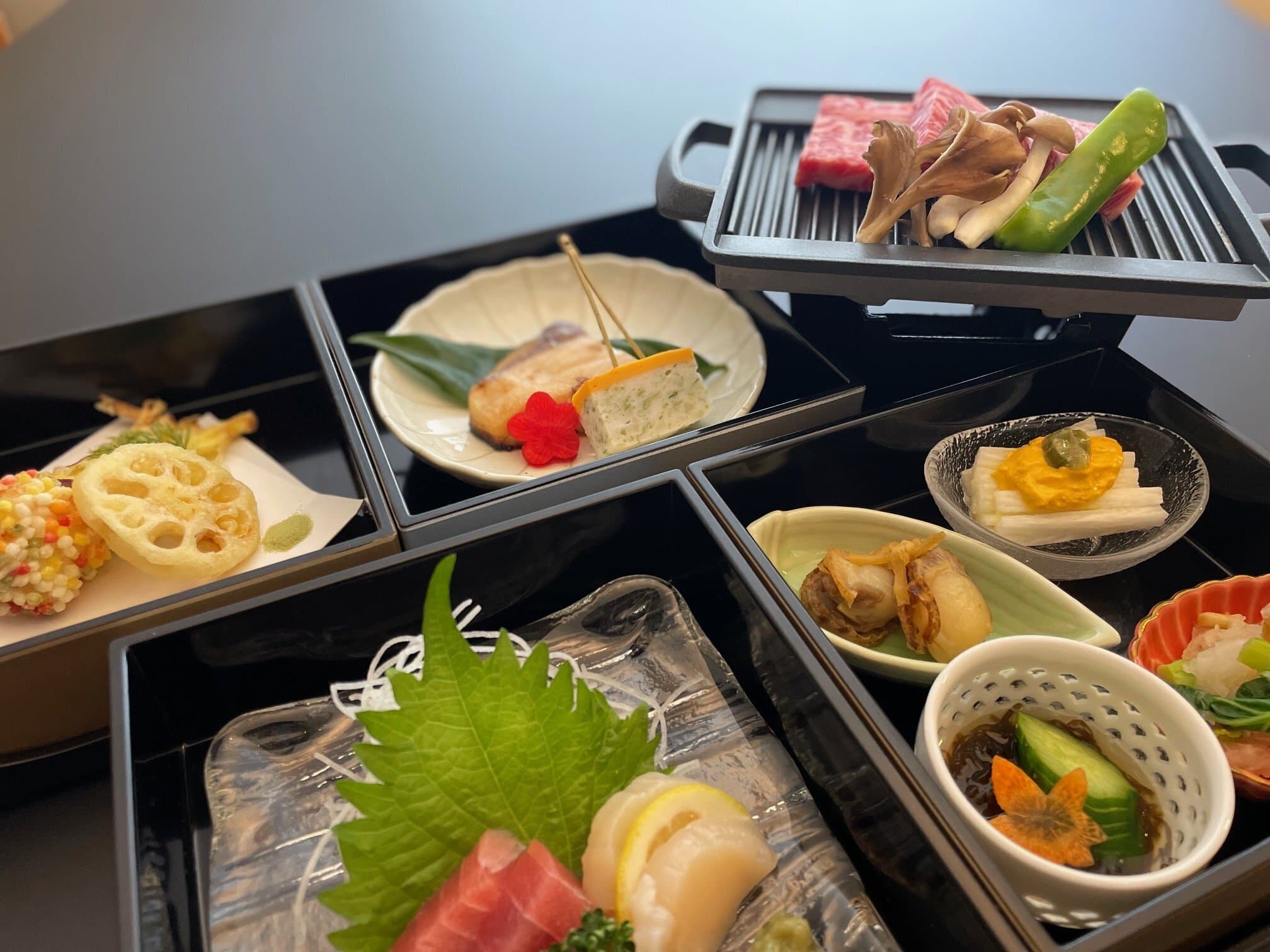 Close-up of kaiseki dinner courses at Kusatsu Onsen Hoshikawa including sashimi, grilled fish and a tabletop wagyu grill
