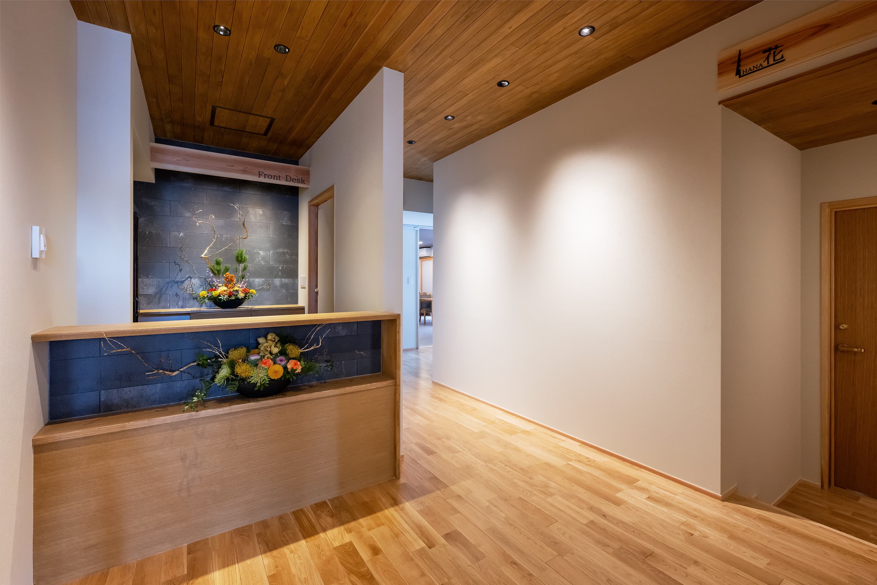 Front desk and lobby at Kusatsu Onsen Hoshikawa with ikebana flower arrangements against a slate-tiled wall and timber ceiling
