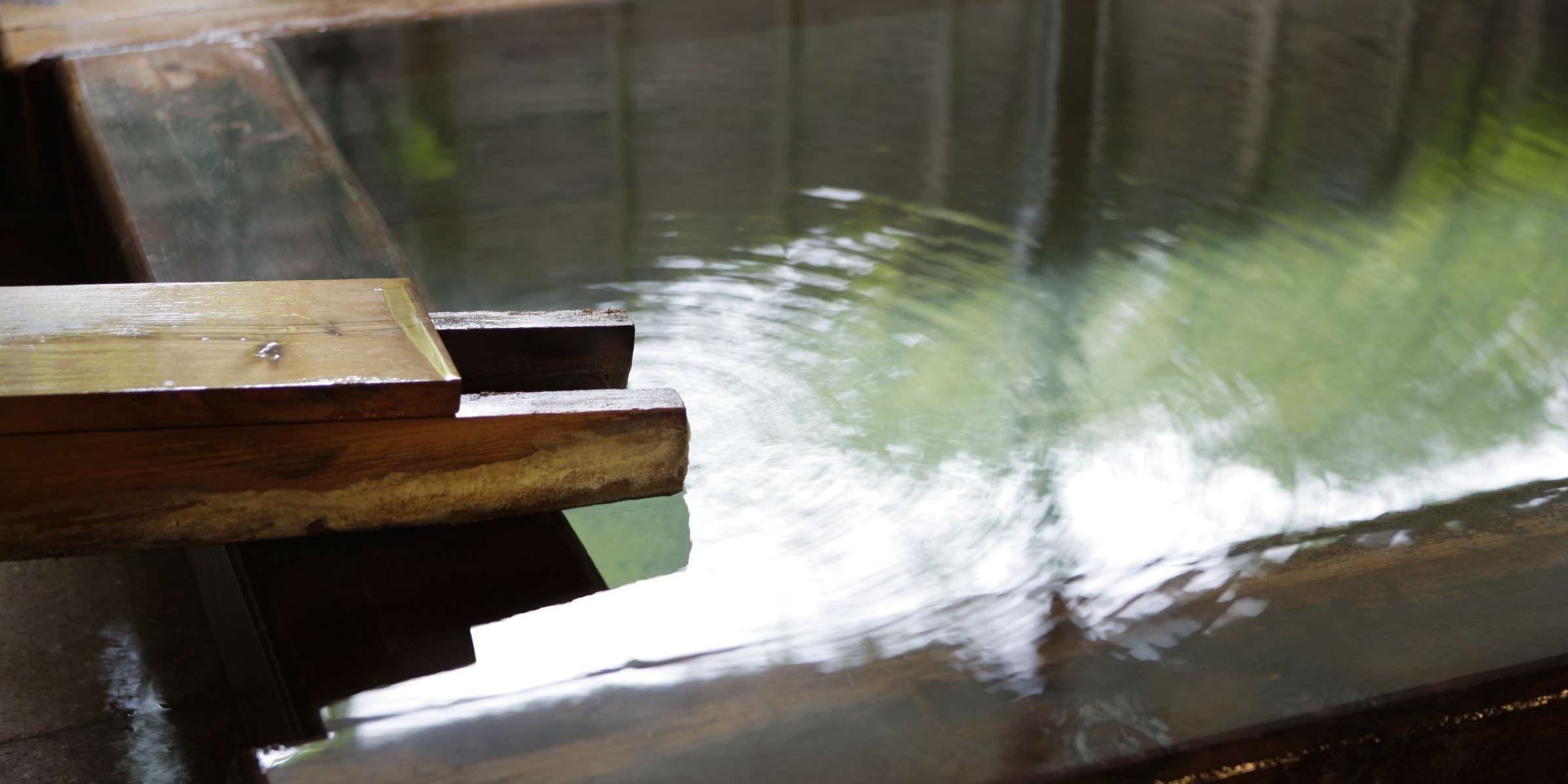 Close-up of milky Kusatsu sulfur spring water flowing into the Wata-no-Yu bath from a wooden spout marked with the Wata-no-Yu name