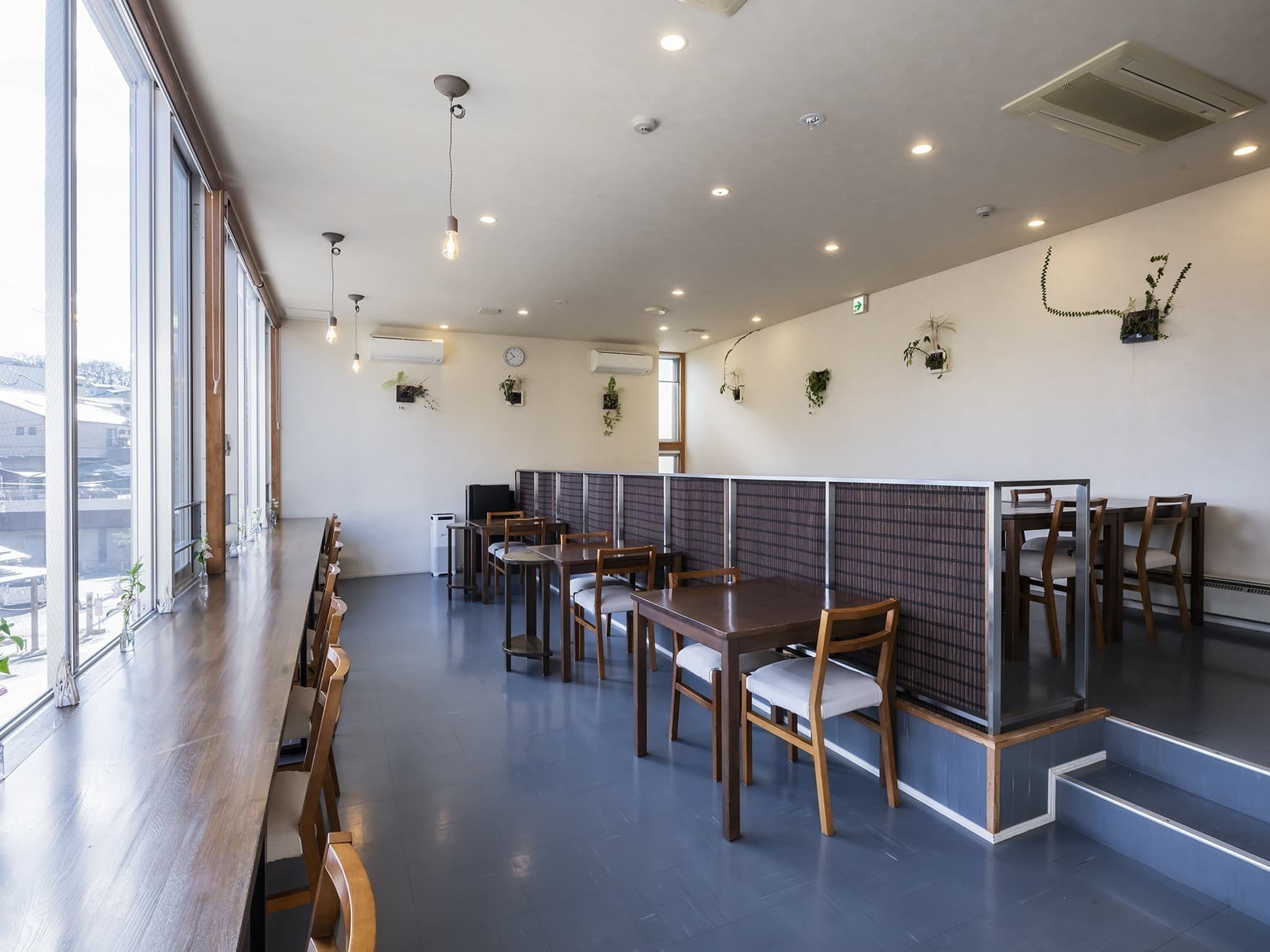Dining cafe space at Wata-no-Yu with wooden tables along a wall of windows overlooking Kusatsu town